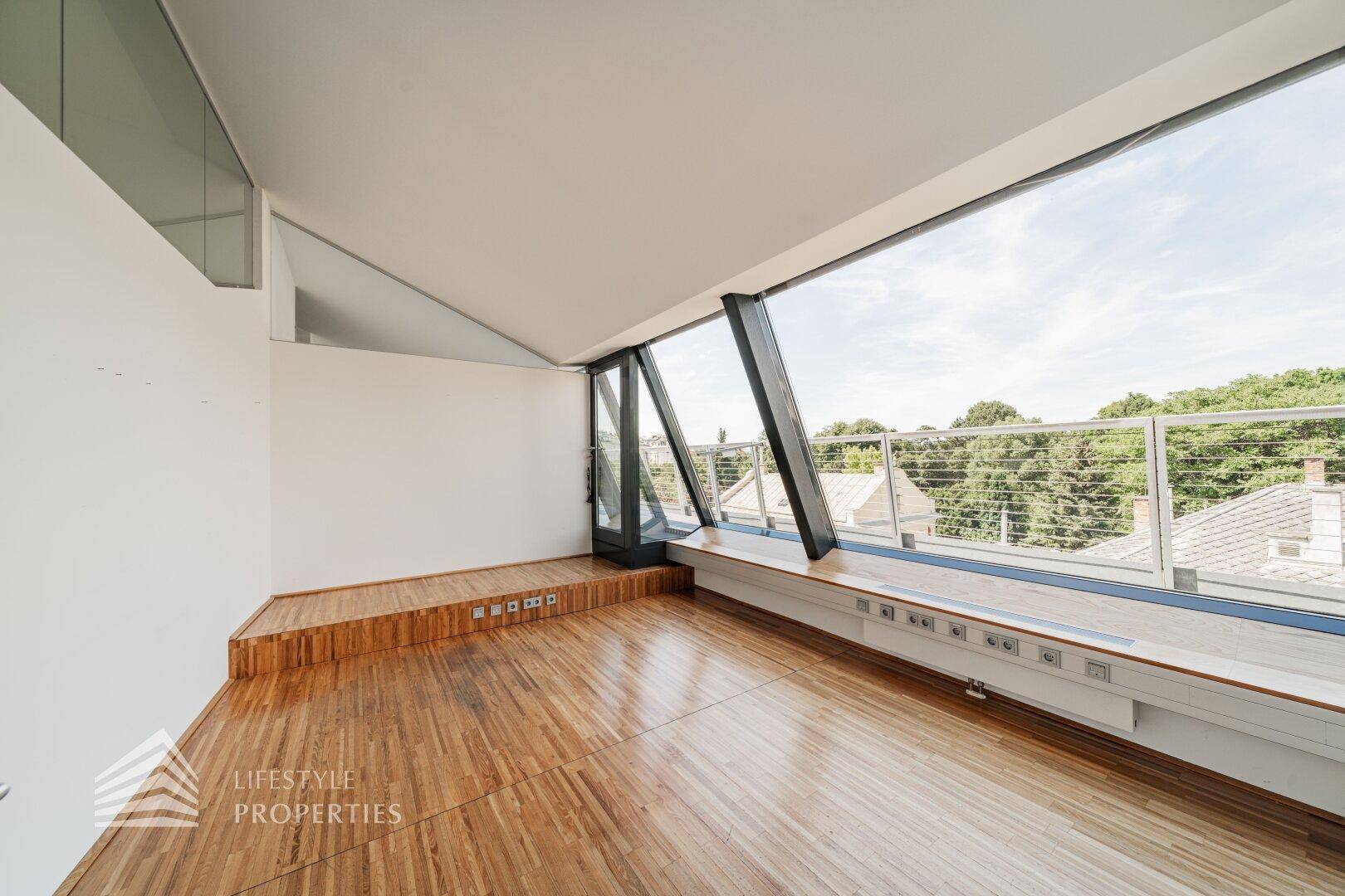 Geräumiger Wohnbereich mit Holzboden und einer erhöhten Plattform am Fenster, die einen weiten Ausblick bietet.