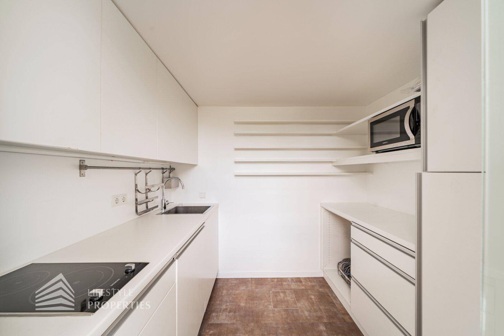 Moderne, kompakte Küche mit weißen Schränken, Induktionskochfeld und Mikrowelle, ideal für kleine Räume.