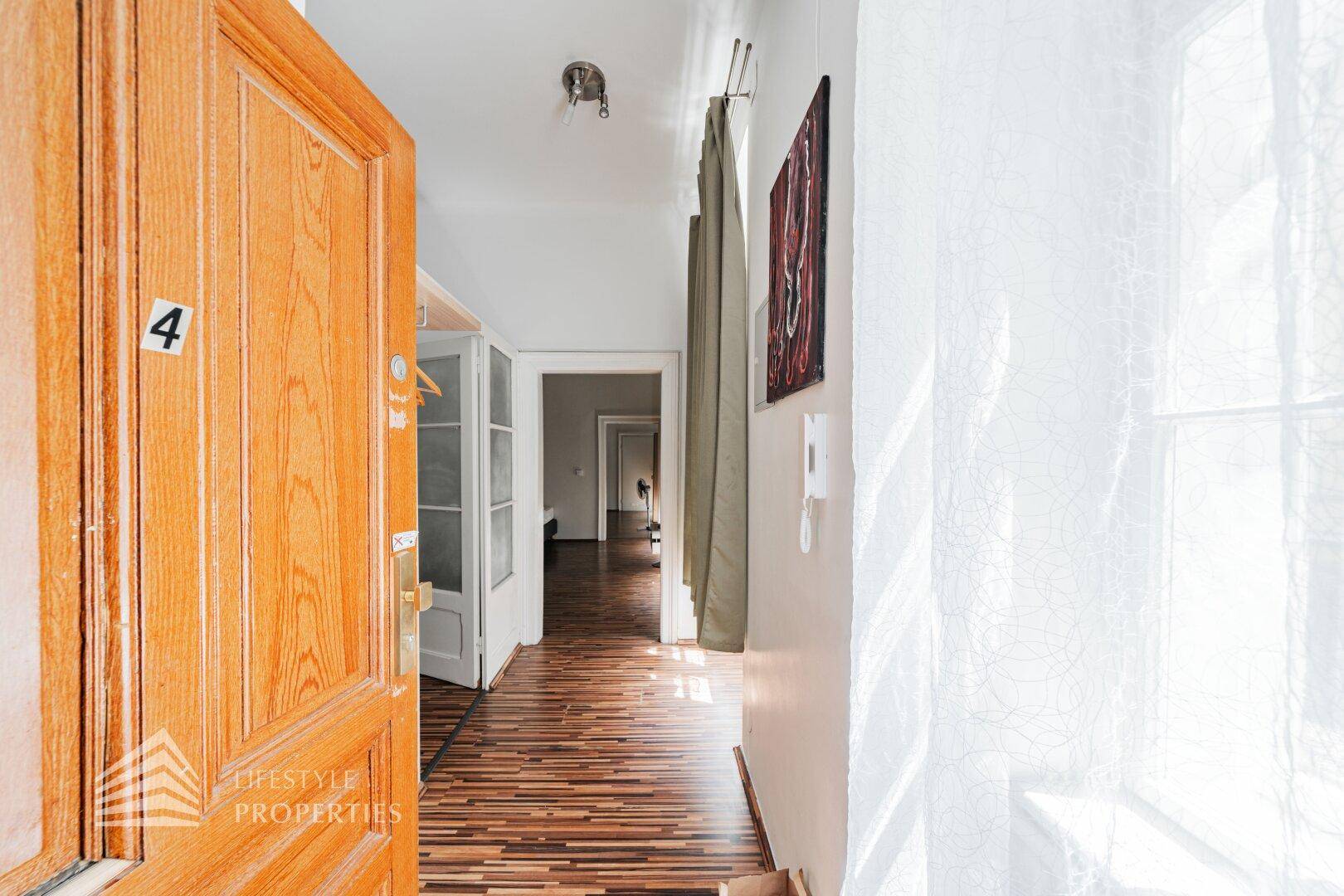 Eingangsbereich der Wohnung mit Holztür und Blick in den hellen Flur mit Holzboden.