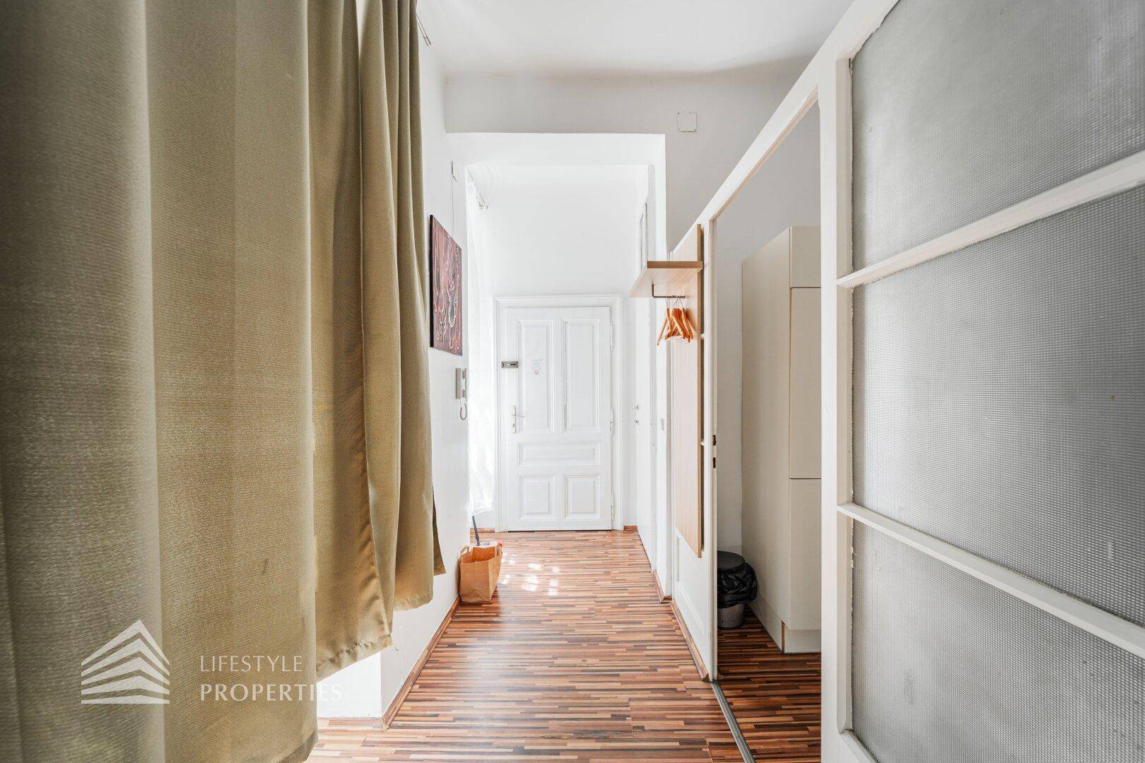Heller Flur mit Holzboden, Spiegel und Garderobe, führt zu weiteren Räumen.