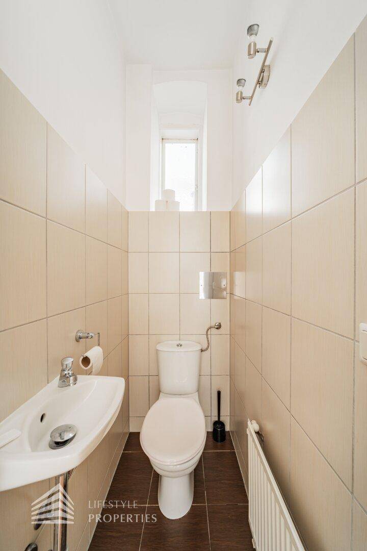 Kleines Gäste-WC mit Toilette, Waschbecken und Fliesen, ausgestattet mit einem schmalen Fenster.