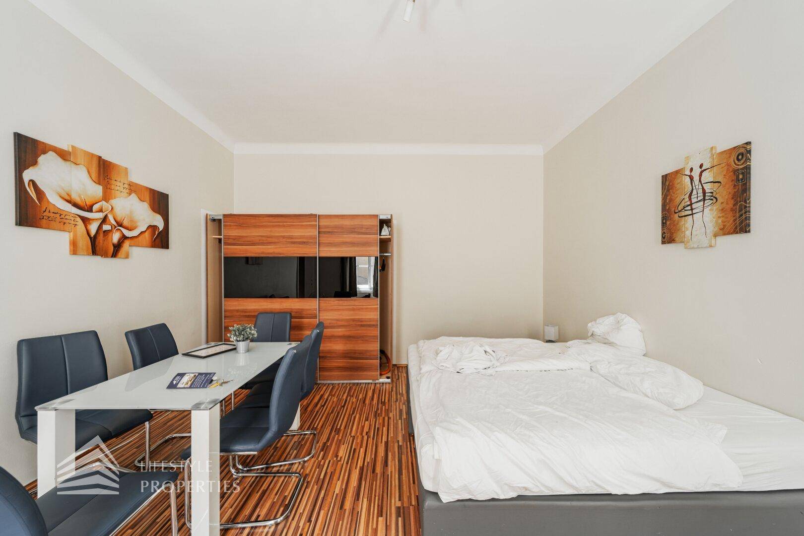Kombinierter Wohn- und Schlafbereich mit Esstisch, Bett und praktischem Holzschrank.