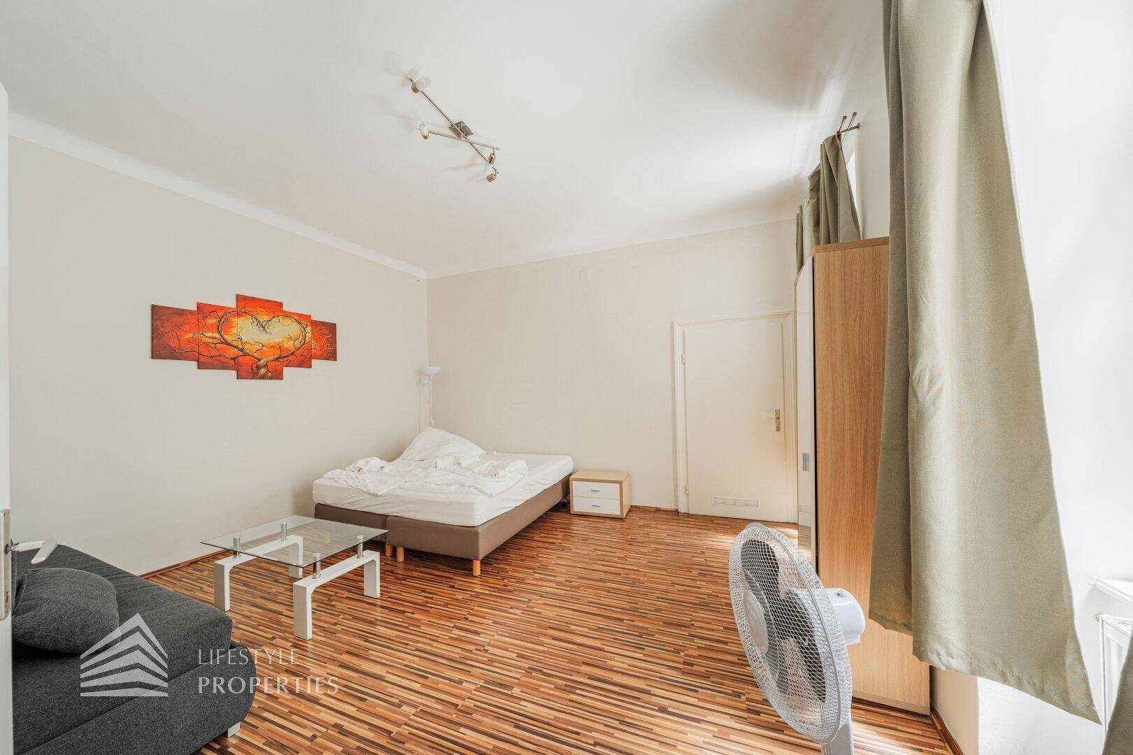 Gemütlicher Wohnbereich mit Bett, Sofa, Couchtisch und Holzboden, ideal für Entspannung.