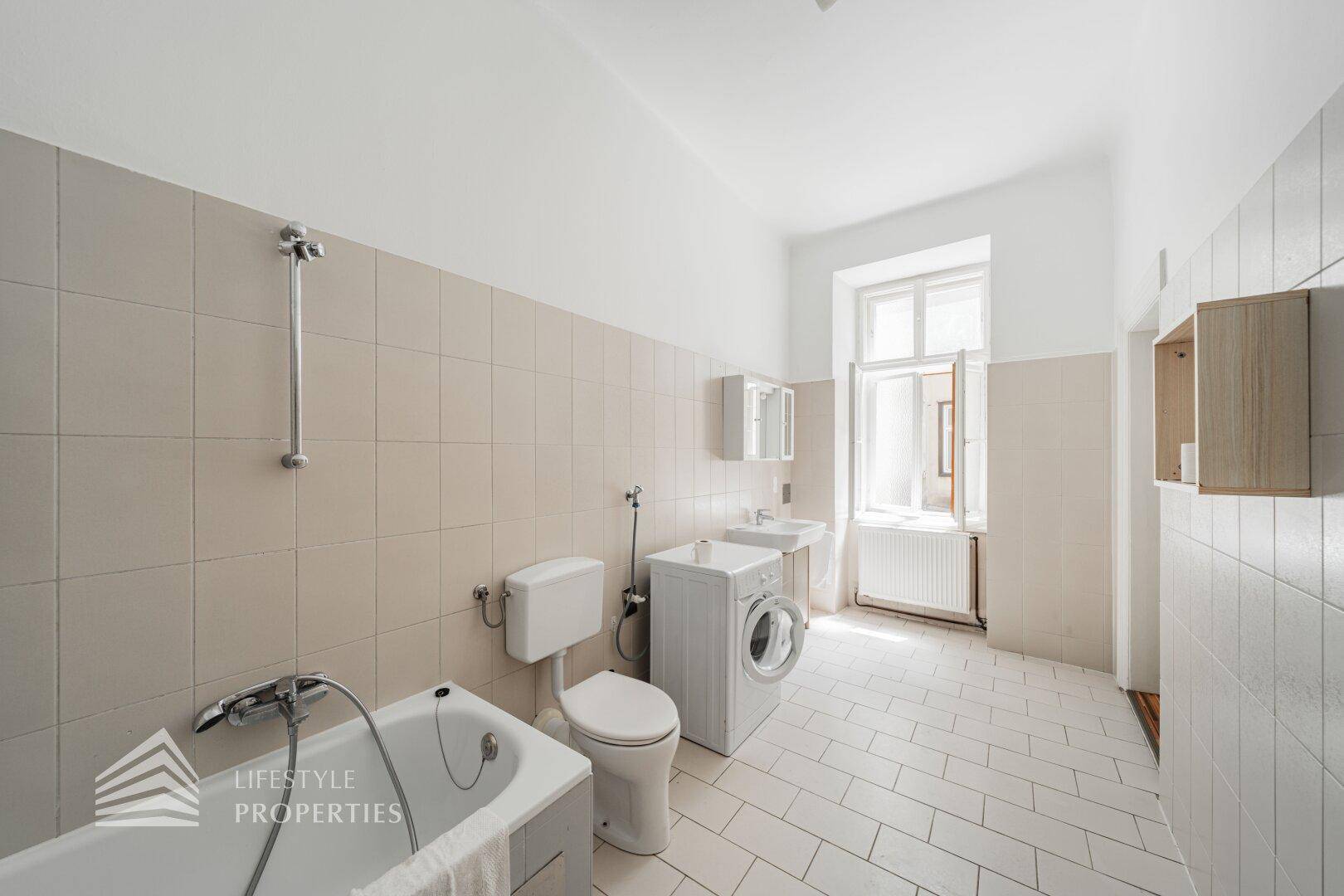 Helles Badezimmer mit Badewanne, WC, Waschbecken und Waschmaschine, ausgestattet mit Fenster.
