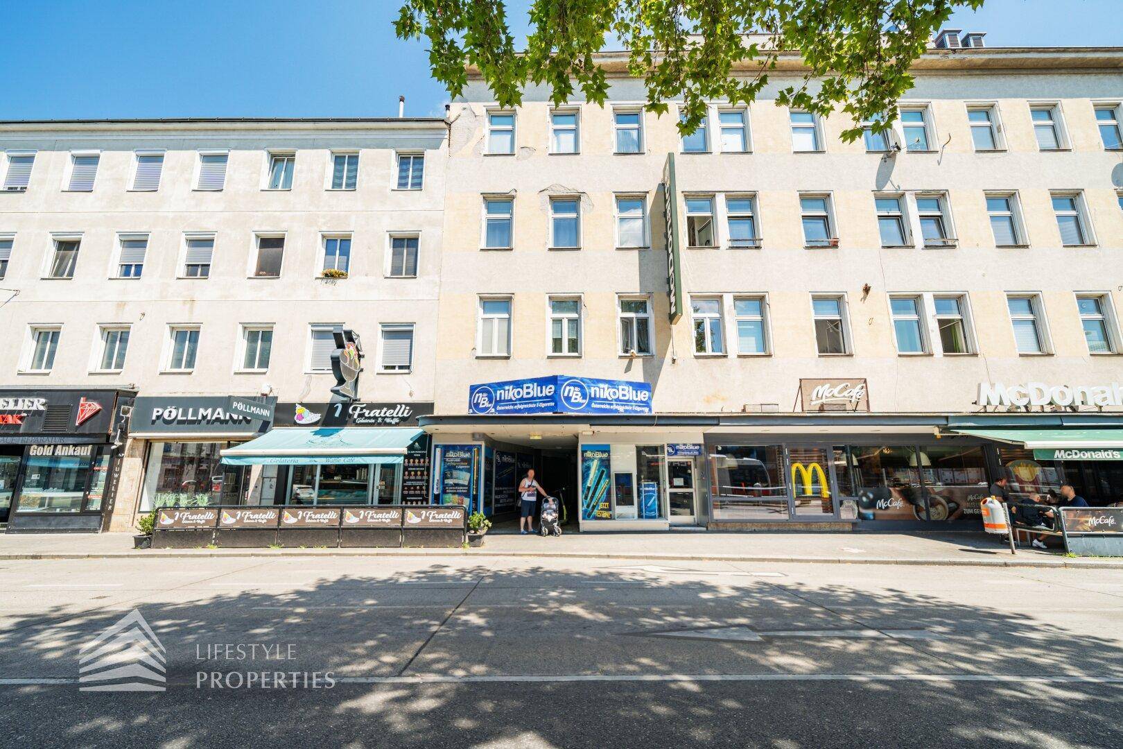 Mehrstöckiges Gebäude an einer belebten Straße mit Geschäften im Erdgeschoss und vielen Fenstern.