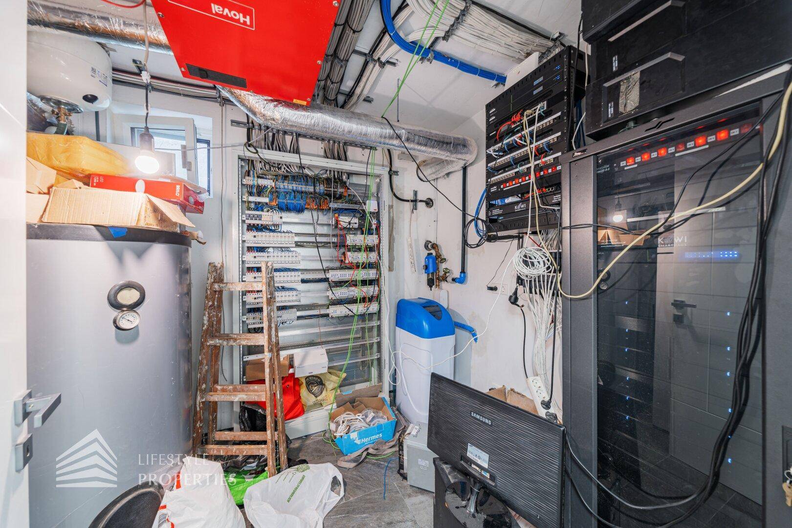 Technikraum im Keller mit Serverracks, Verkabelung und Heizungsanlage.