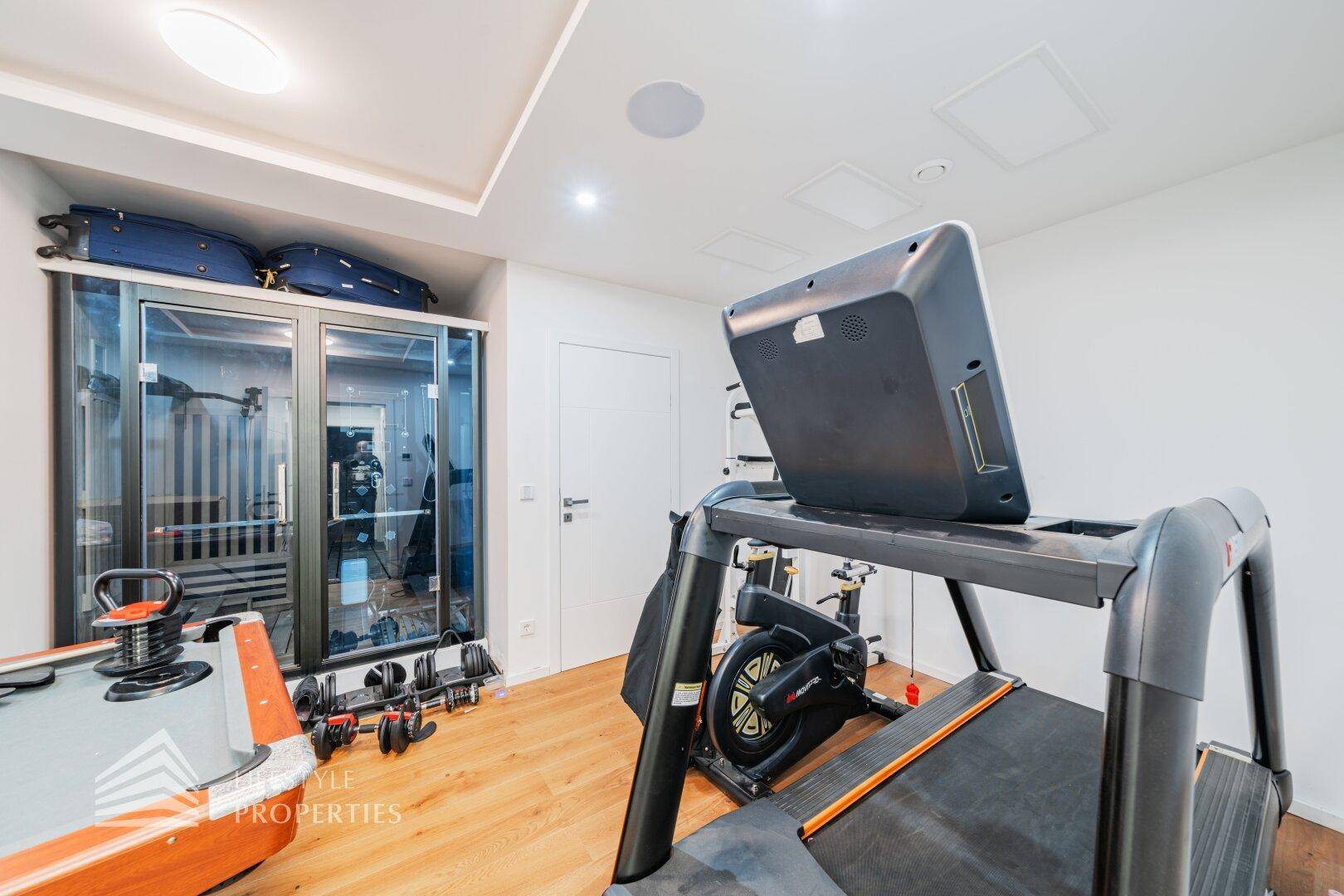 Privater Fitnessraum mit Laufband, Trainingsgeräten und Holzboden für sportliche Aktivitäten.