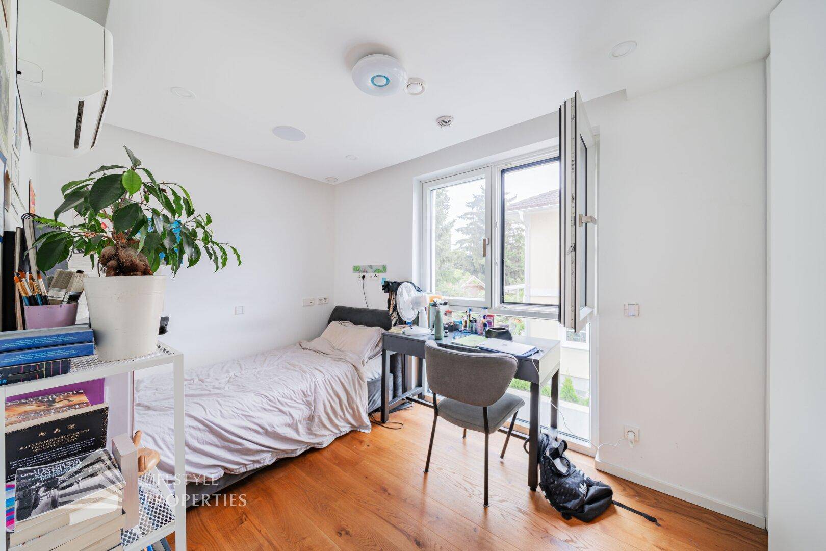 Helles Schlafzimmer mit Einzelbett, Schreibtisch und Blick aus dem Fenster.