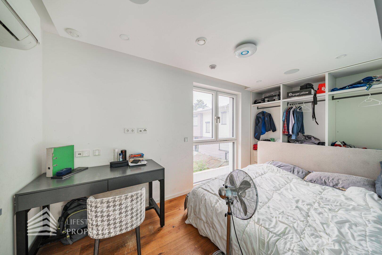Schlafzimmer mit Holzboden, Schreibtisch und integriertem Kleiderschrank.