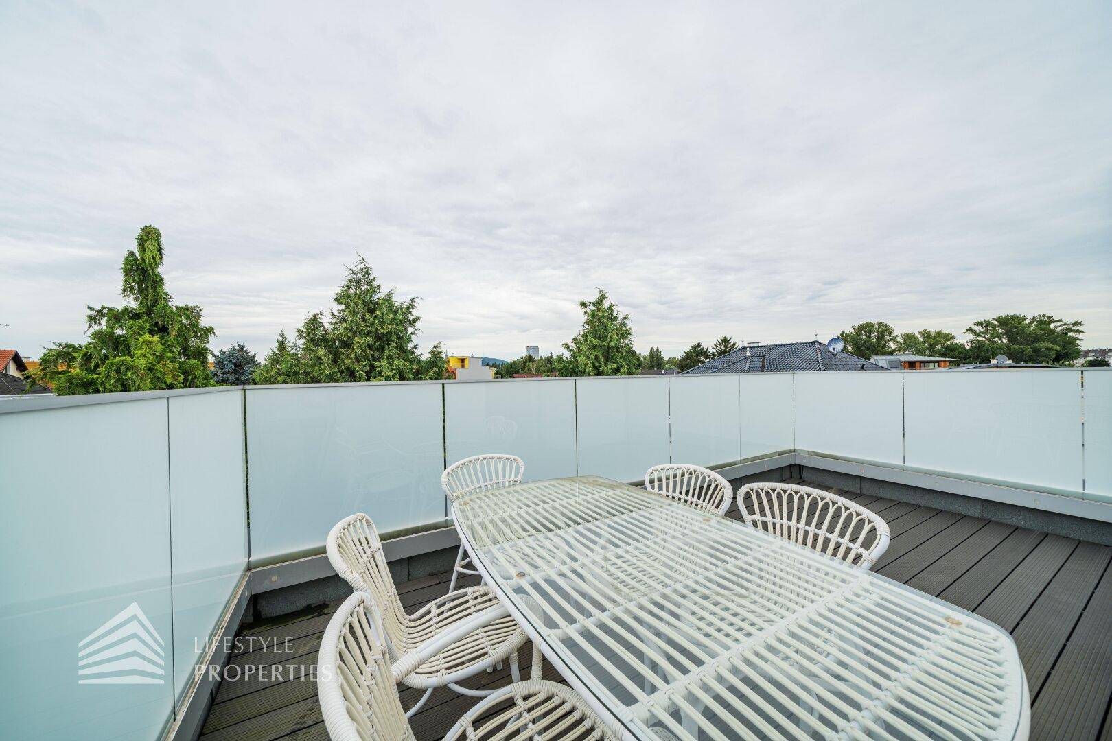 Geräumige Dachterrasse mit Holzboden und modernen Glasgeländern, möbliert für Entspannung.