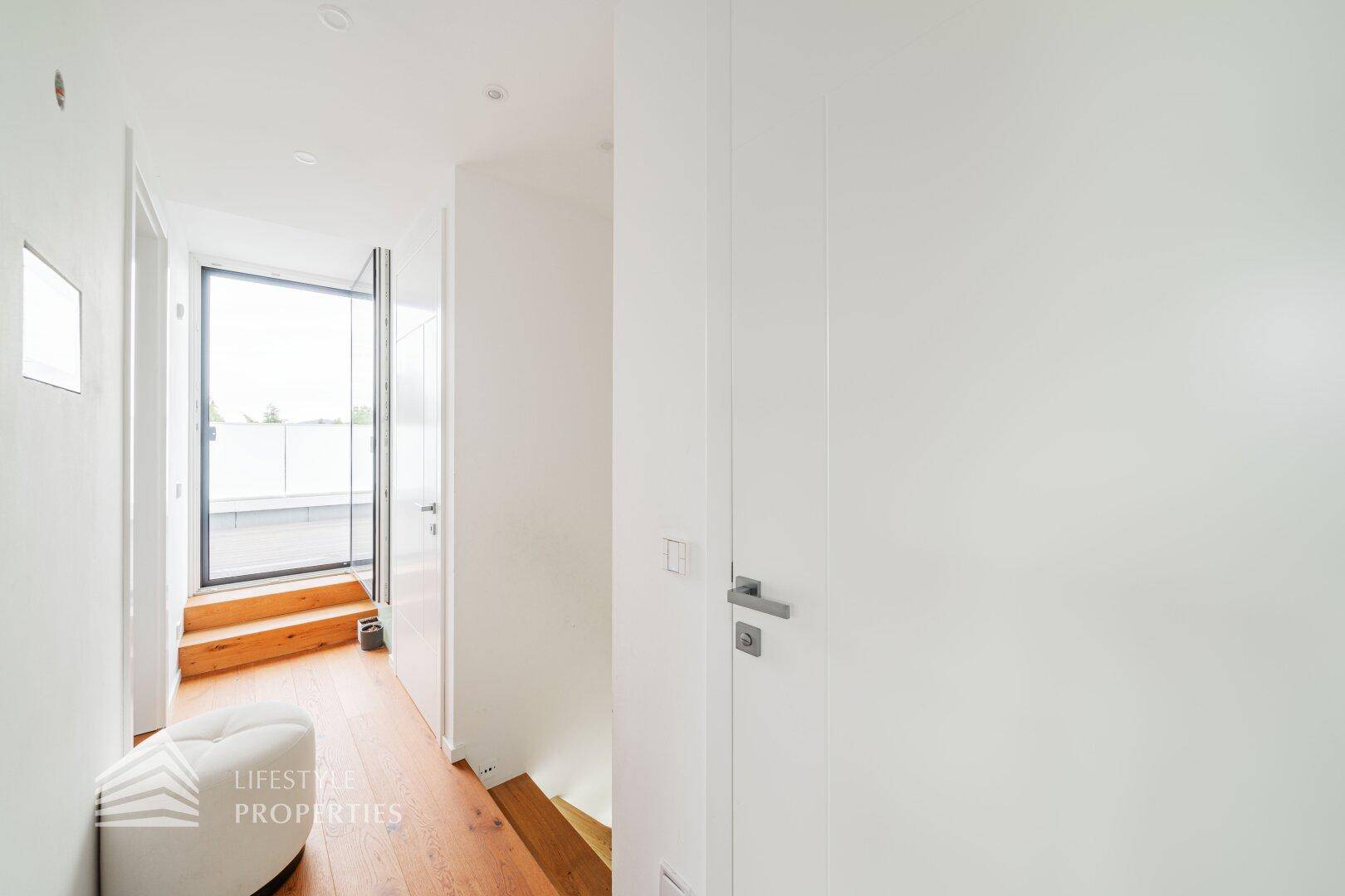Heller Flur mit Holztreppe und Zugang zur Dachterrasse durch eine Glastür.