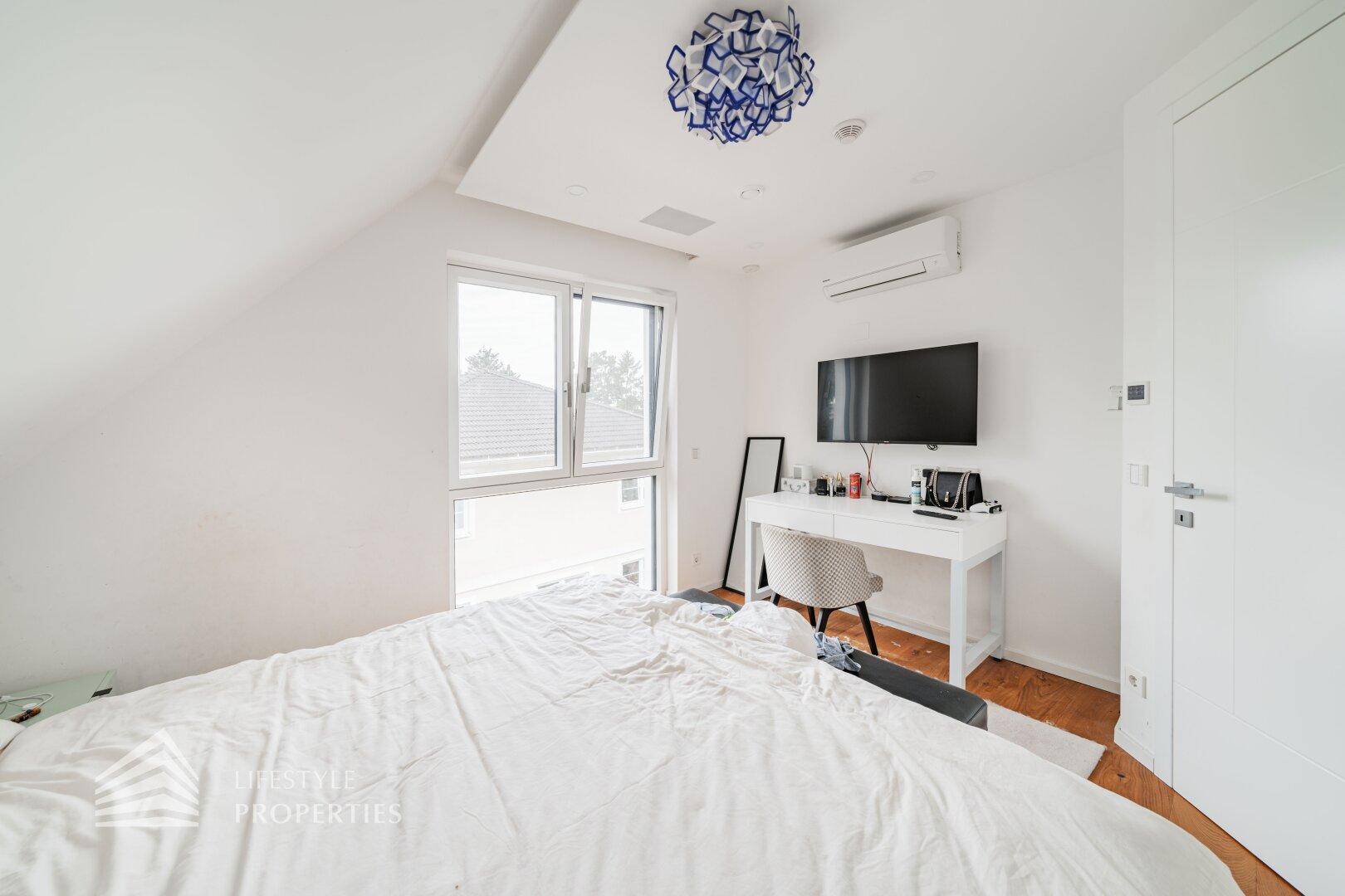 Helles Schlafzimmer im Dachgeschoss mit Klimaanlage, Schreibtisch und Blick nach draußen.
