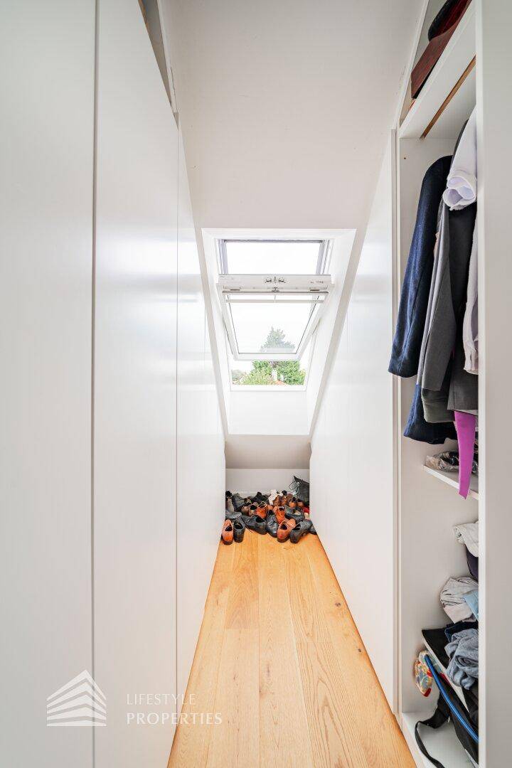 Schmaler begehbarer Kleiderschrank mit Dachfenster und Stauraum für Schuhe und Kleidung.