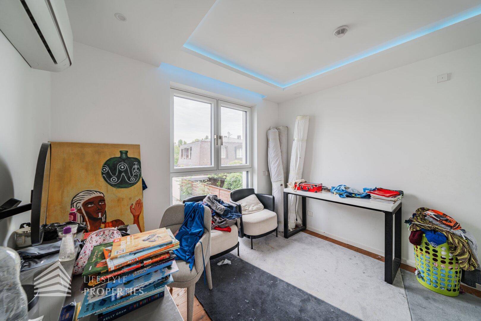 Helles Zimmer mit großem Fenster, Klimaanlage und moderner Deckenbeleuchtung.