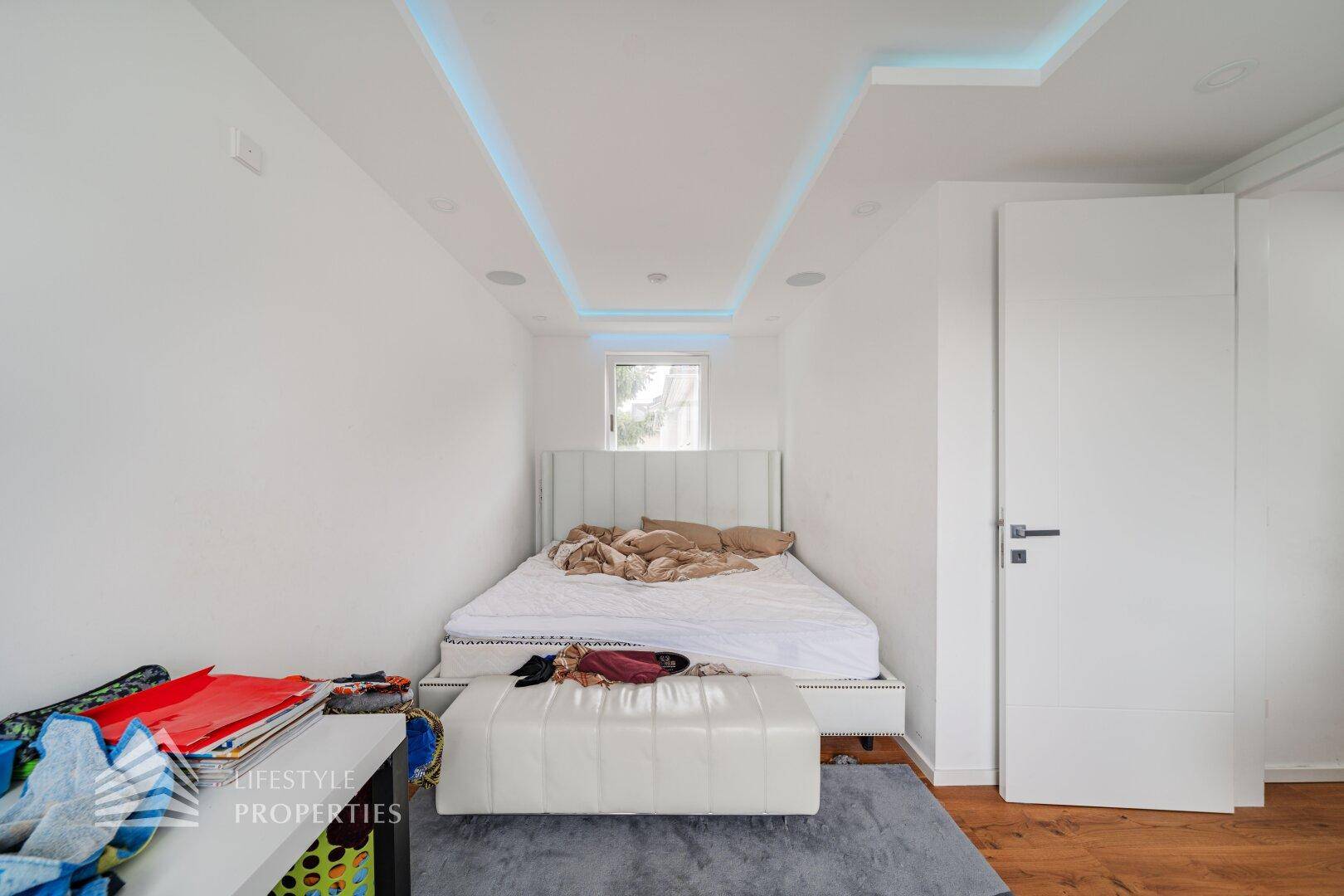 Schlafzimmer mit modernem Bett, Deckenbeleuchtung und hellem Ambiente.