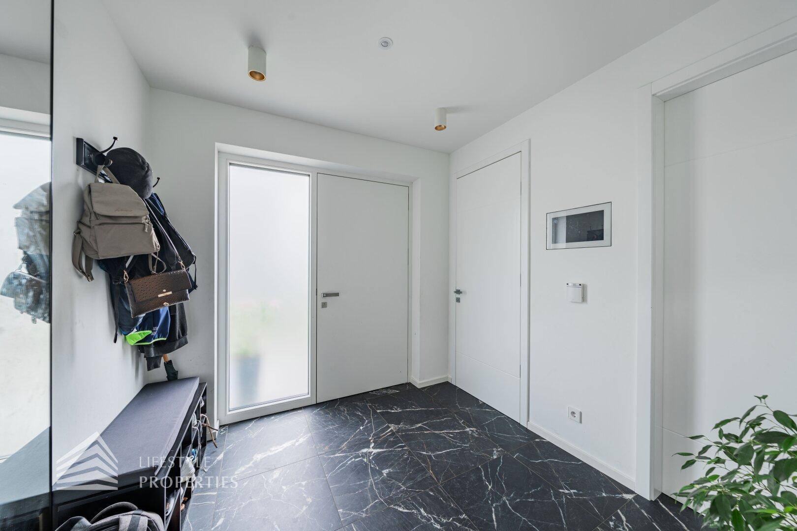 Heller Eingangsbereich mit dunklem Marmorboden, Garderobe und moderner Tür.