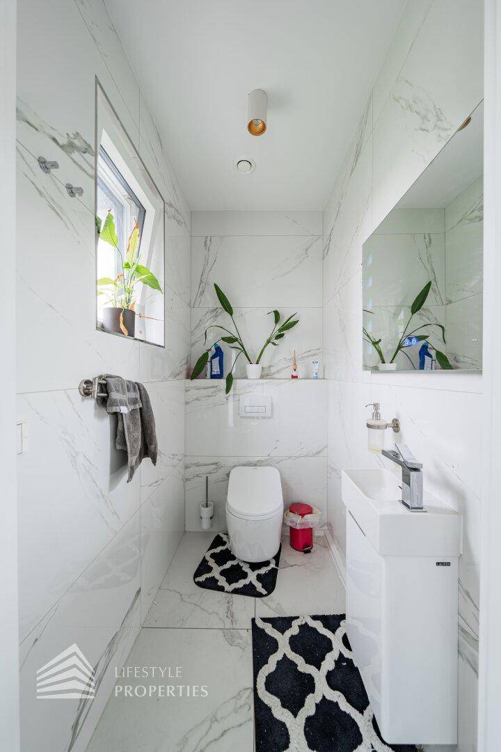 Modernes Gäste-WC mit weißen Marmorfliesen, Fenster und minimalistischem Waschbecken.