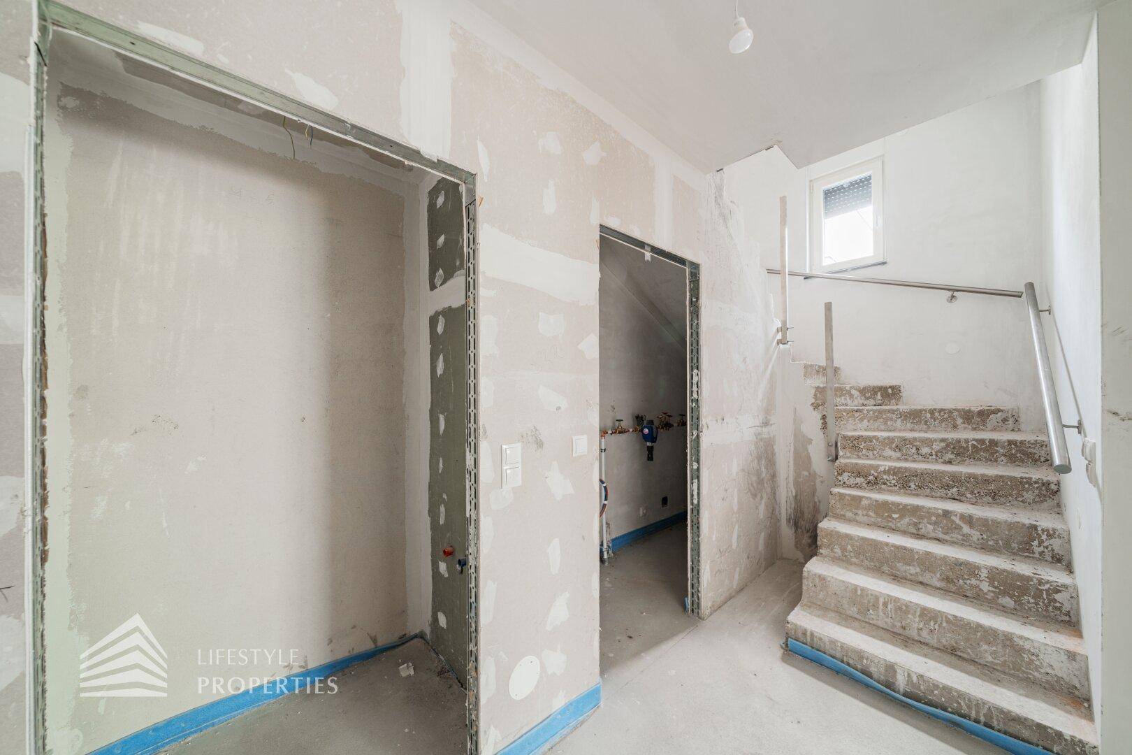 Unfertiger Flur mit Betontreppe und Metallgeländer, führt zu weiteren Räumen.