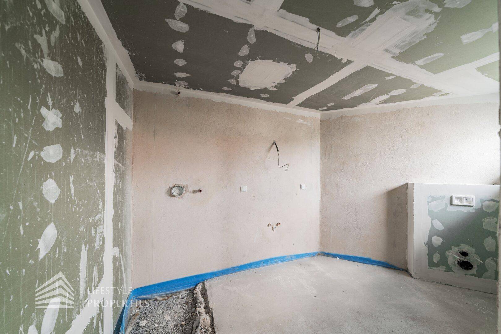 Unfertiger Raum mit sichtbaren Installationen und vorbereiteten Wänden für den weiteren Ausbau.