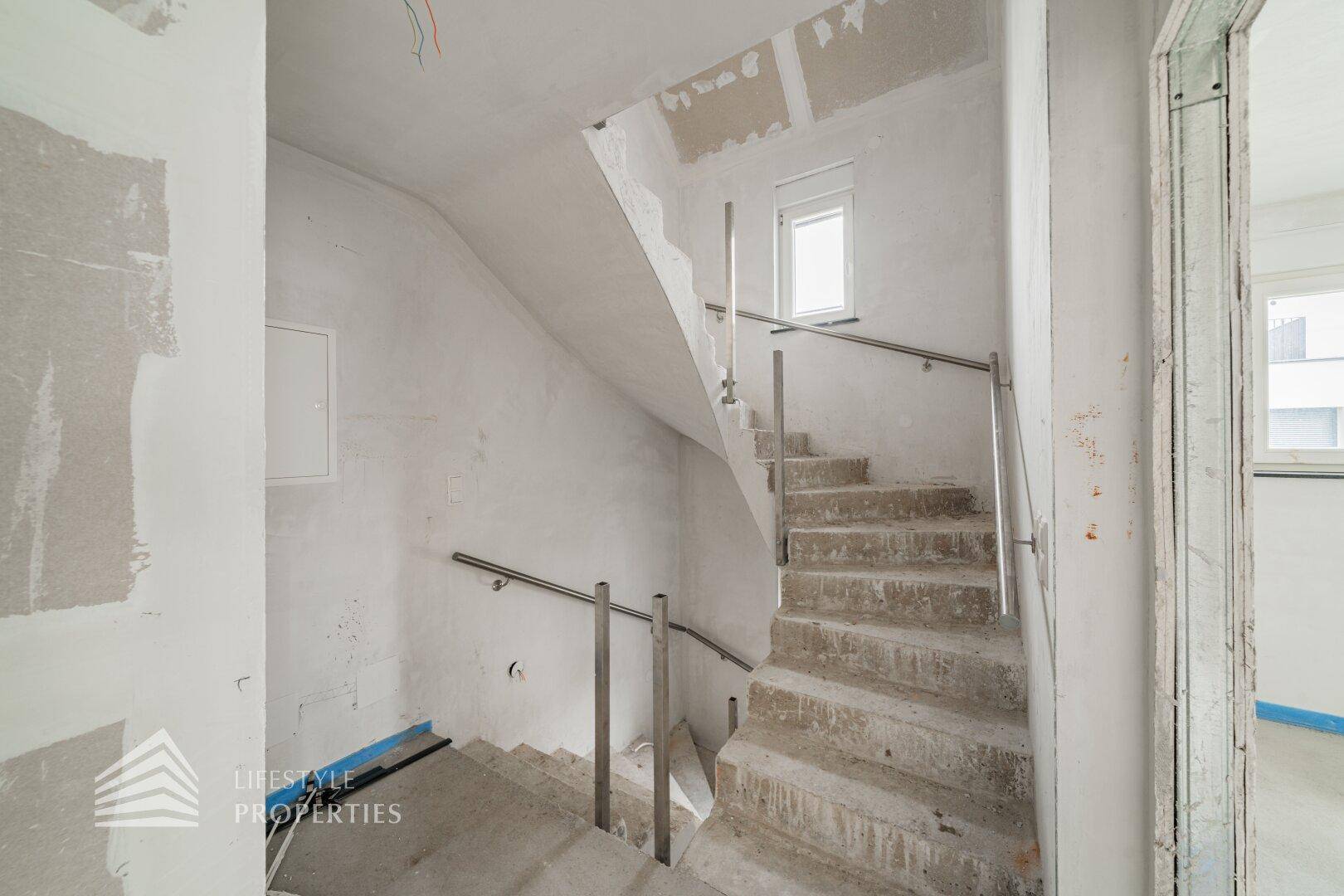 Unfertiges Treppenhaus mit Betontreppe und Metallgeländer, führt in die oberen Stockwerke.