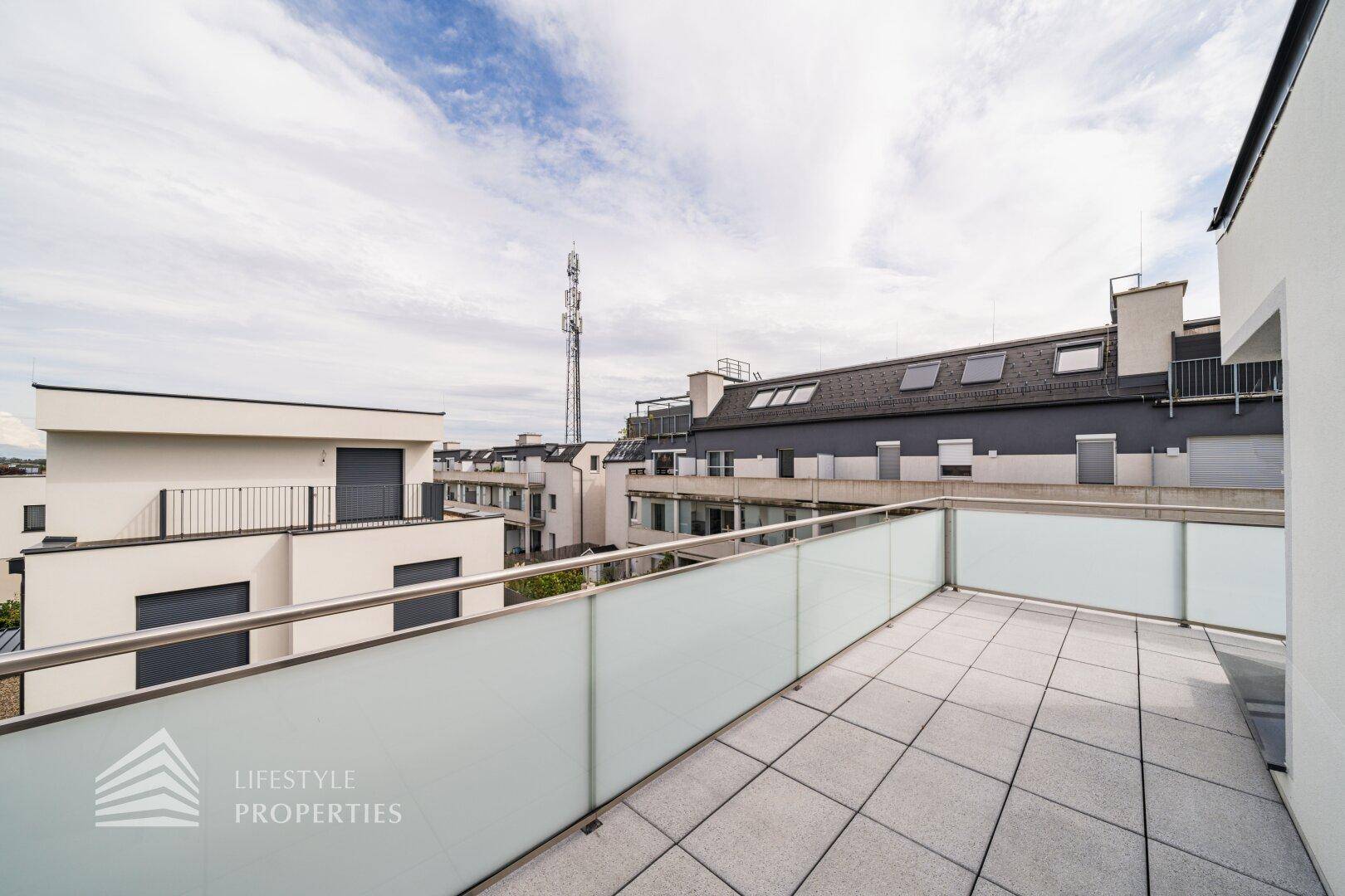 Großzügige Dachterrasse mit Fliesenboden und Glasgeländer, bietet einen weiten Blick über die Dächer.