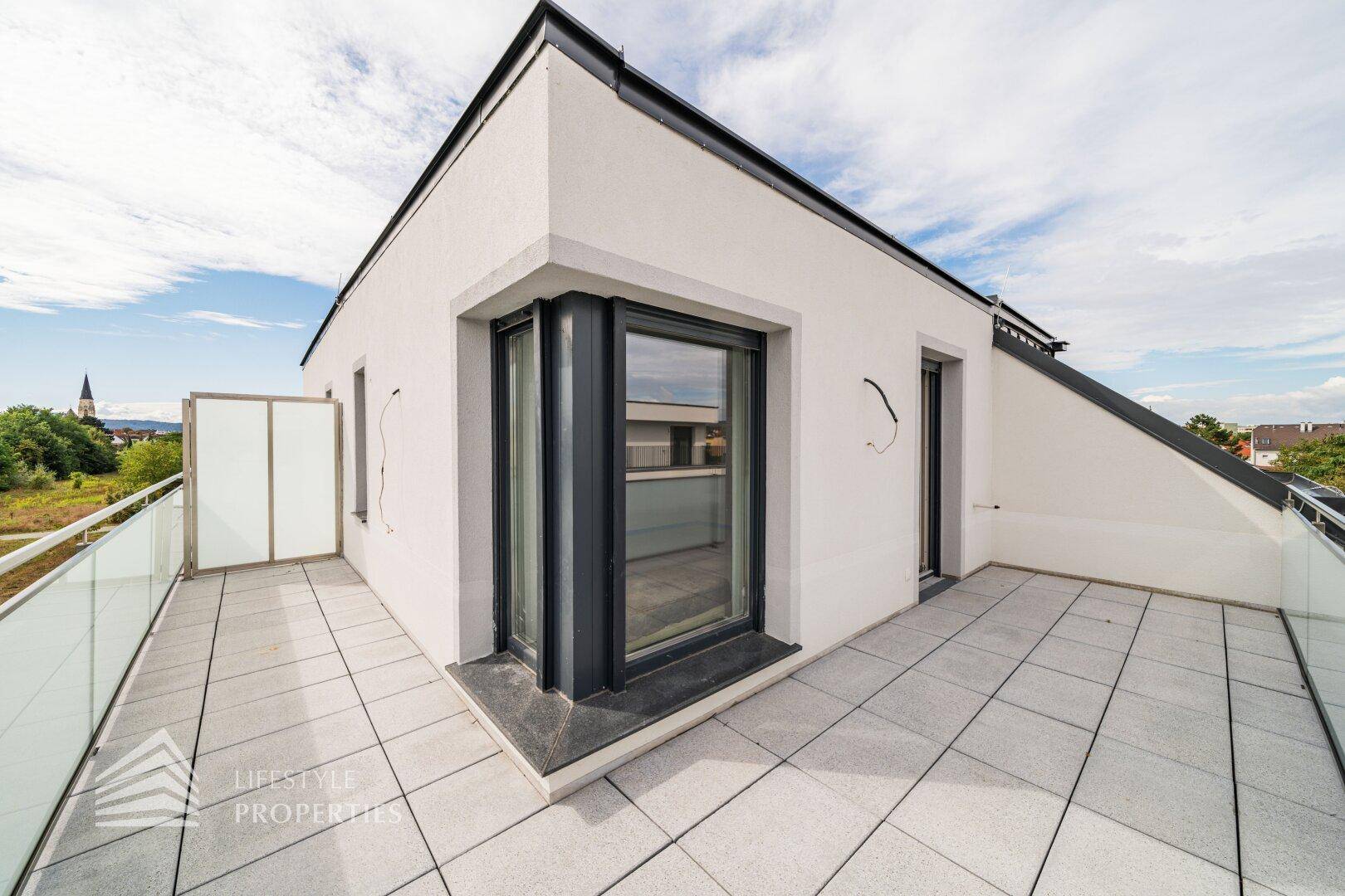 Eckbereich der Dachterrasse mit Fliesenboden und moderner Fassade des Gebäudes.