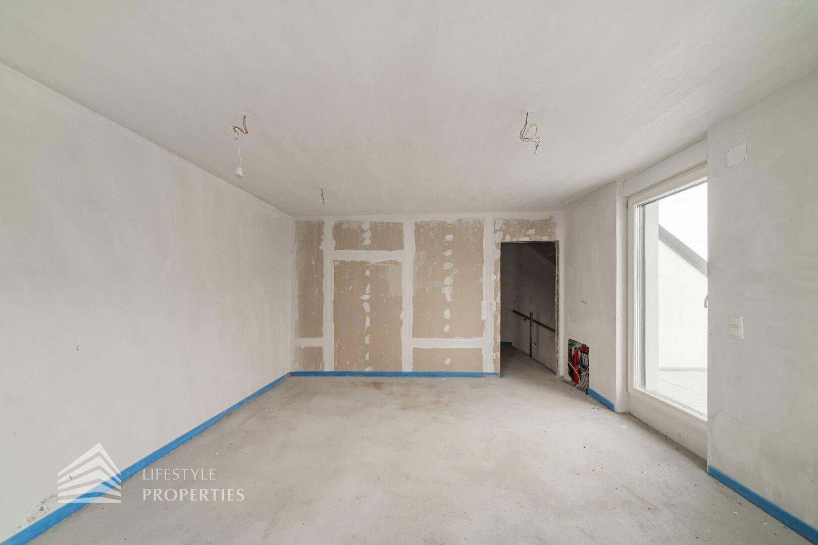 Unfertiger Wohnraum mit Rohbetonboden und Zugang zu einem Außenbereich, bereit für den Ausbau.