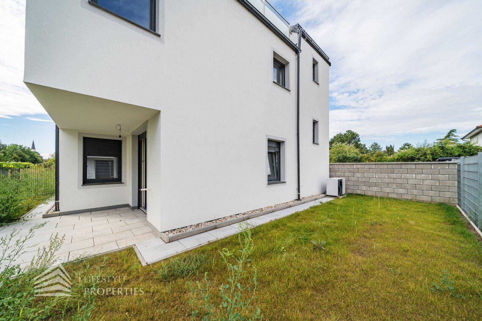 Moderne Hausfassade mit kleiner Terrasse und Rasenfläche, ideal für entspannte Stunden im Freien.