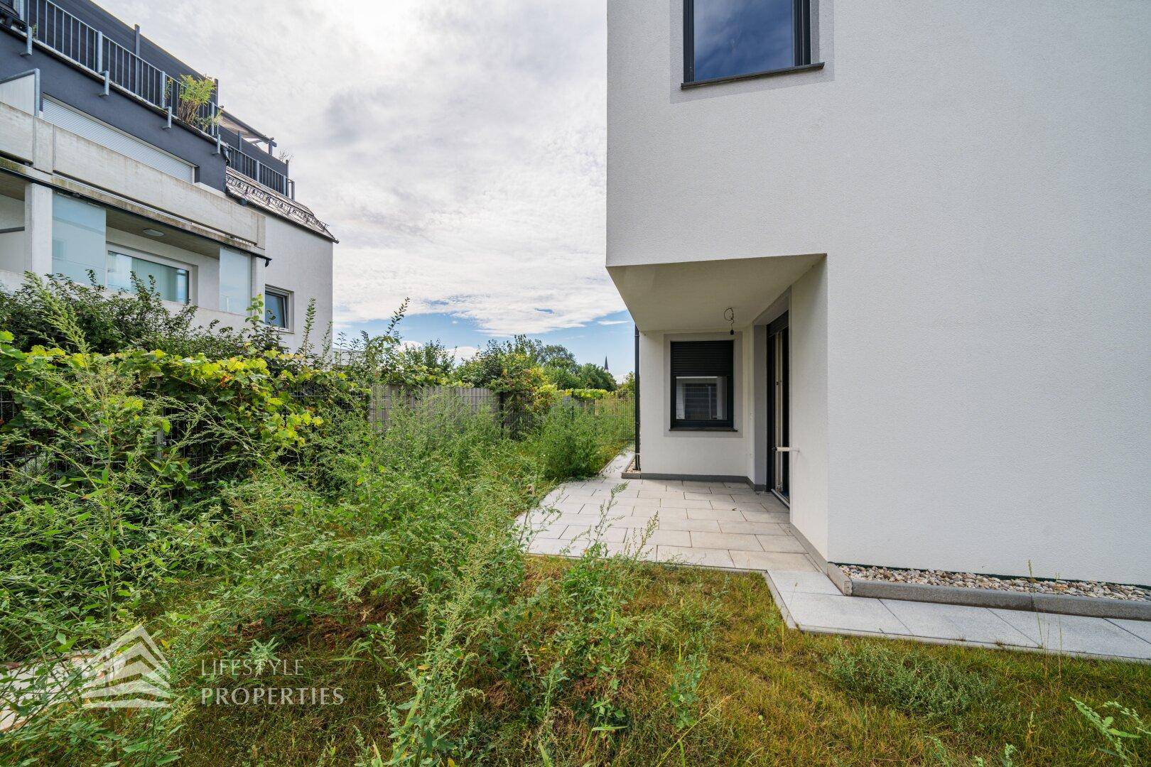 Seitlicher Blick auf das moderne Haus mit gepflasterter Terrasse und naturbelassener Grünfläche.