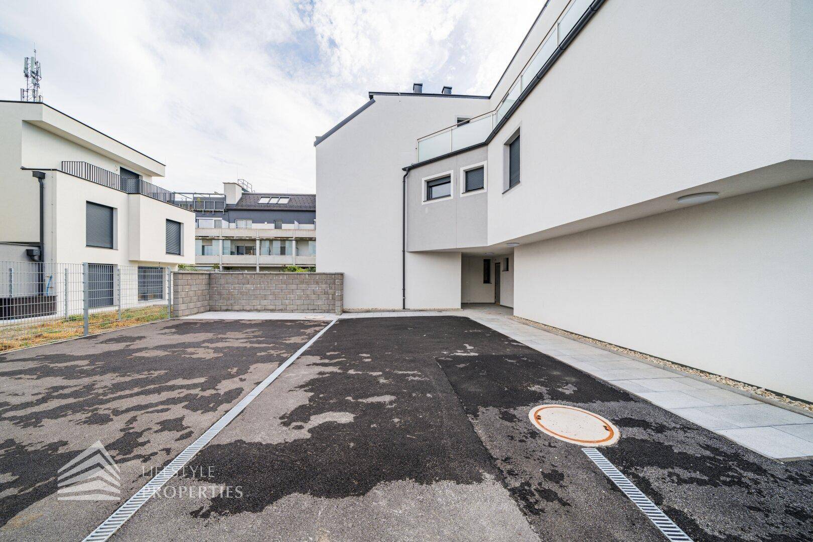 Ansicht des modernen Gebäudes mit asphaltiertem Parkplatz und Zugangsbereich.