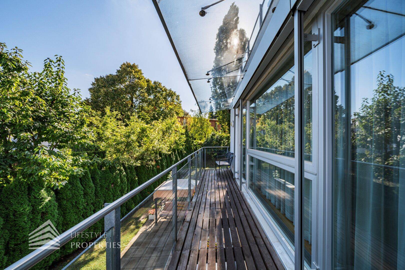 Langer Holzbalkon mit Glasgeländer und Blick ins Grüne.
