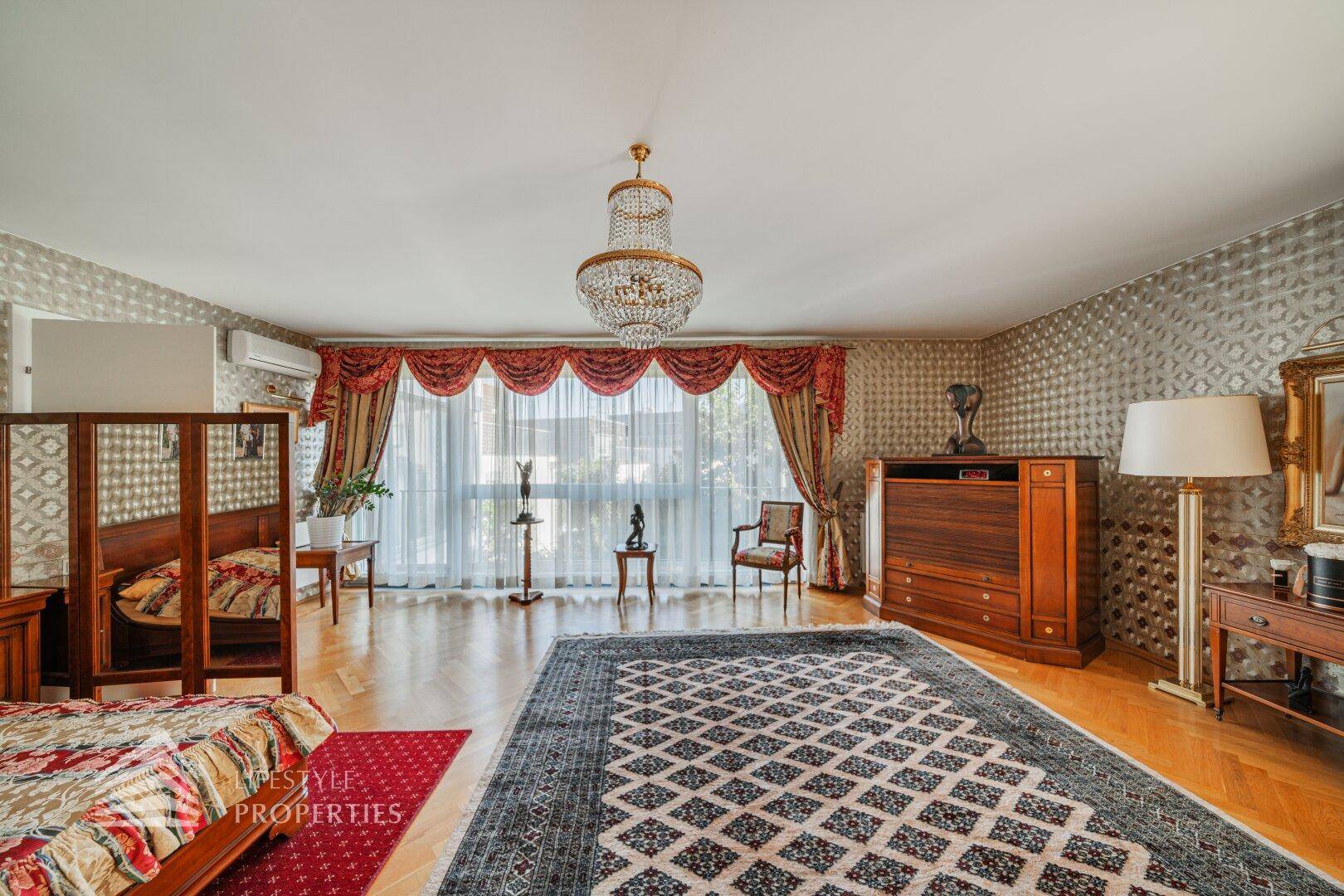 Großes Schlafzimmer mit elegantem Kronleuchter, Parkettboden und großen Fenstern.