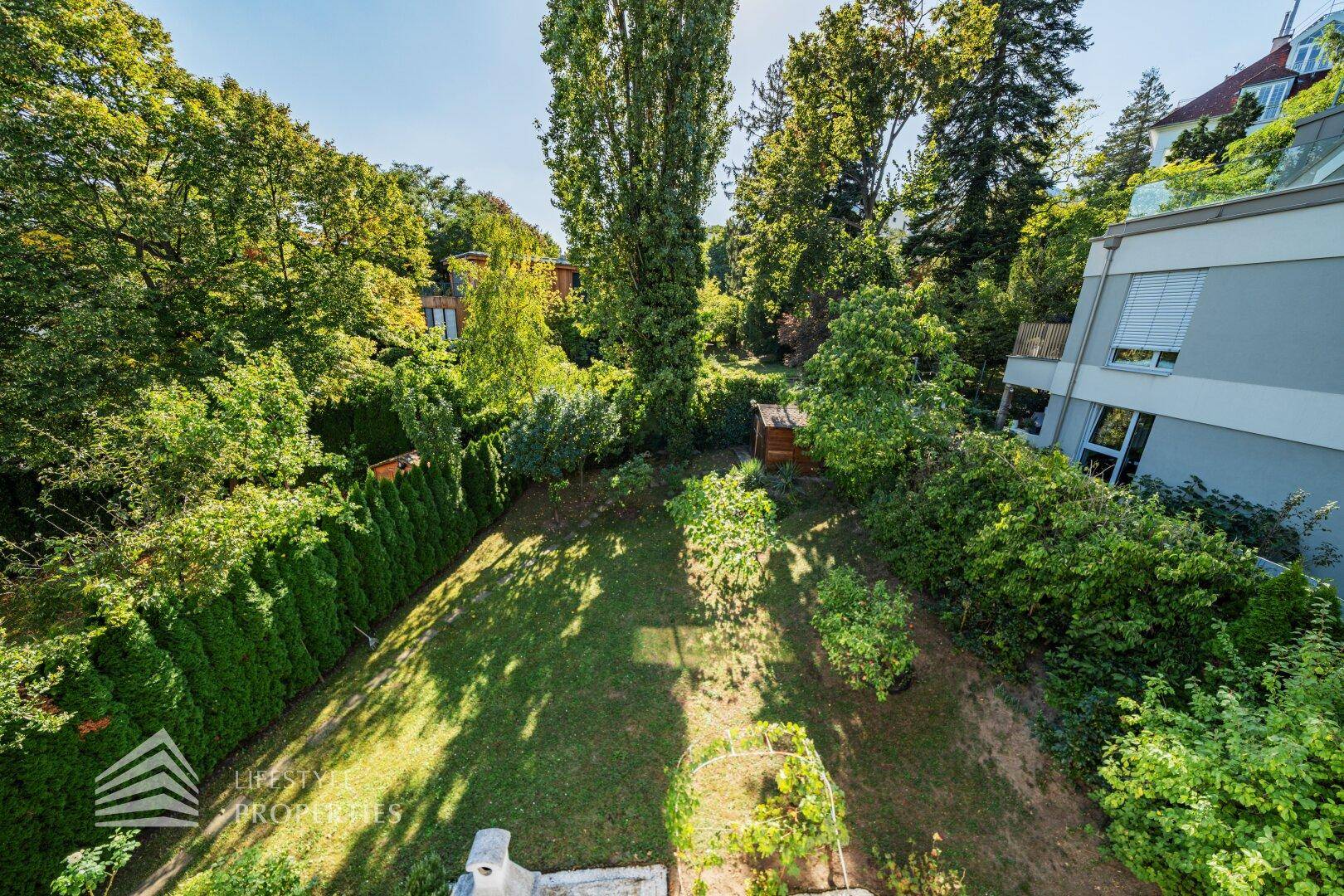 Blick von oben auf den weitläufigen Garten mit üppiger Vegetation und Gartenhaus.