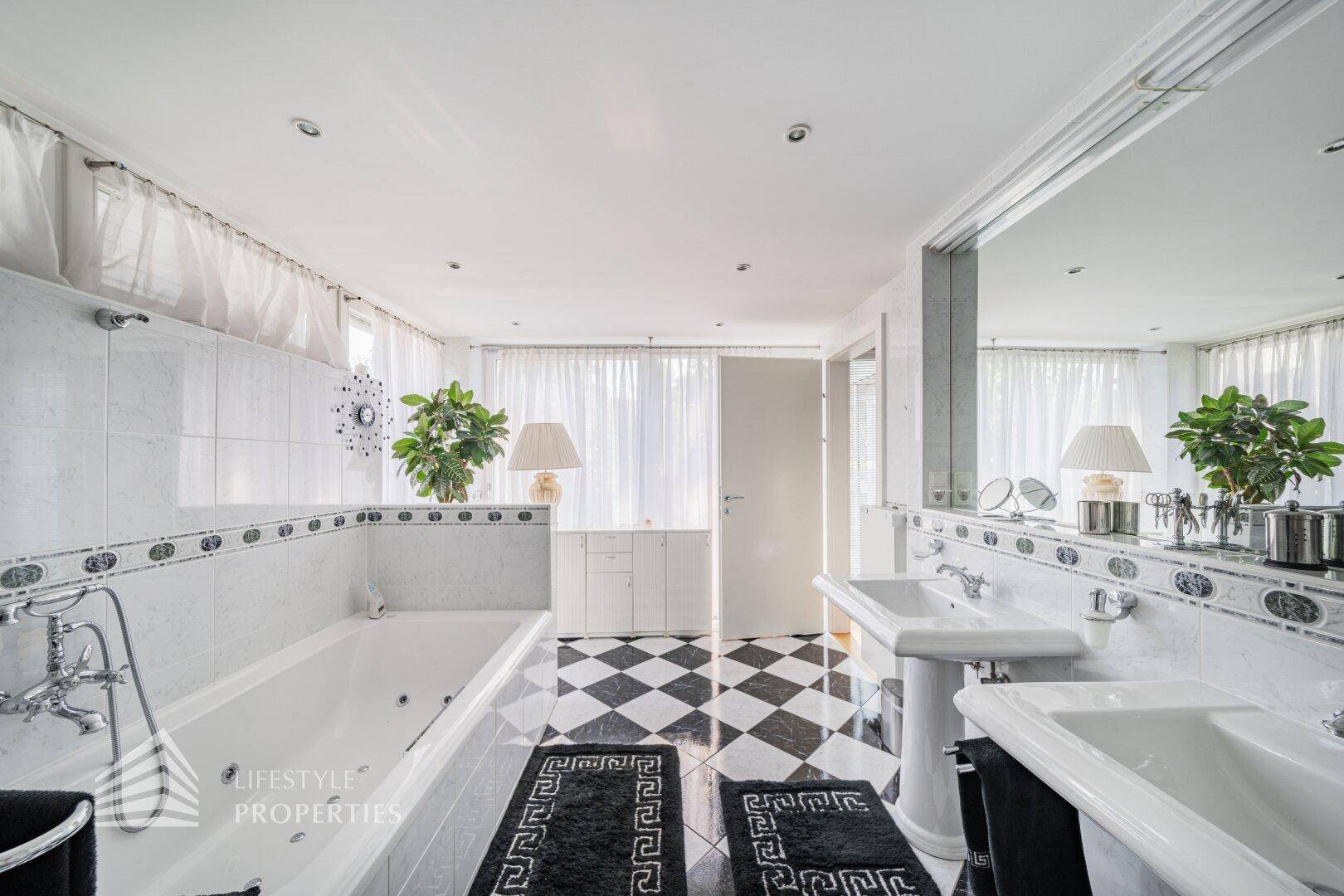 Luxuriöses Badezimmer mit Doppelwaschbecken, Badewanne und schwarz-weißem Fliesenboden.