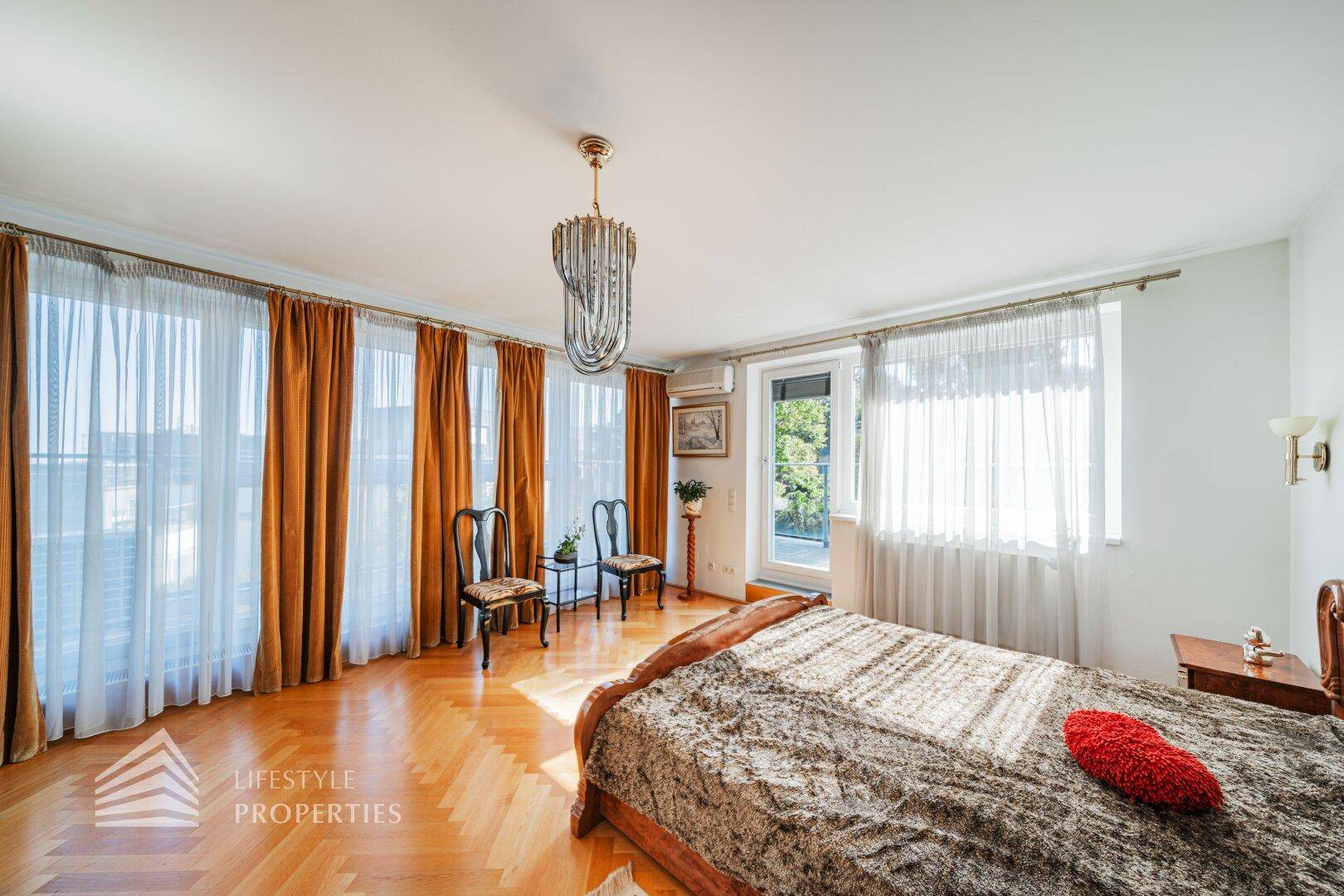 Geräumiges Schlafzimmer mit Parkettboden, großen Fenstern und Zugang zum Balkon.
