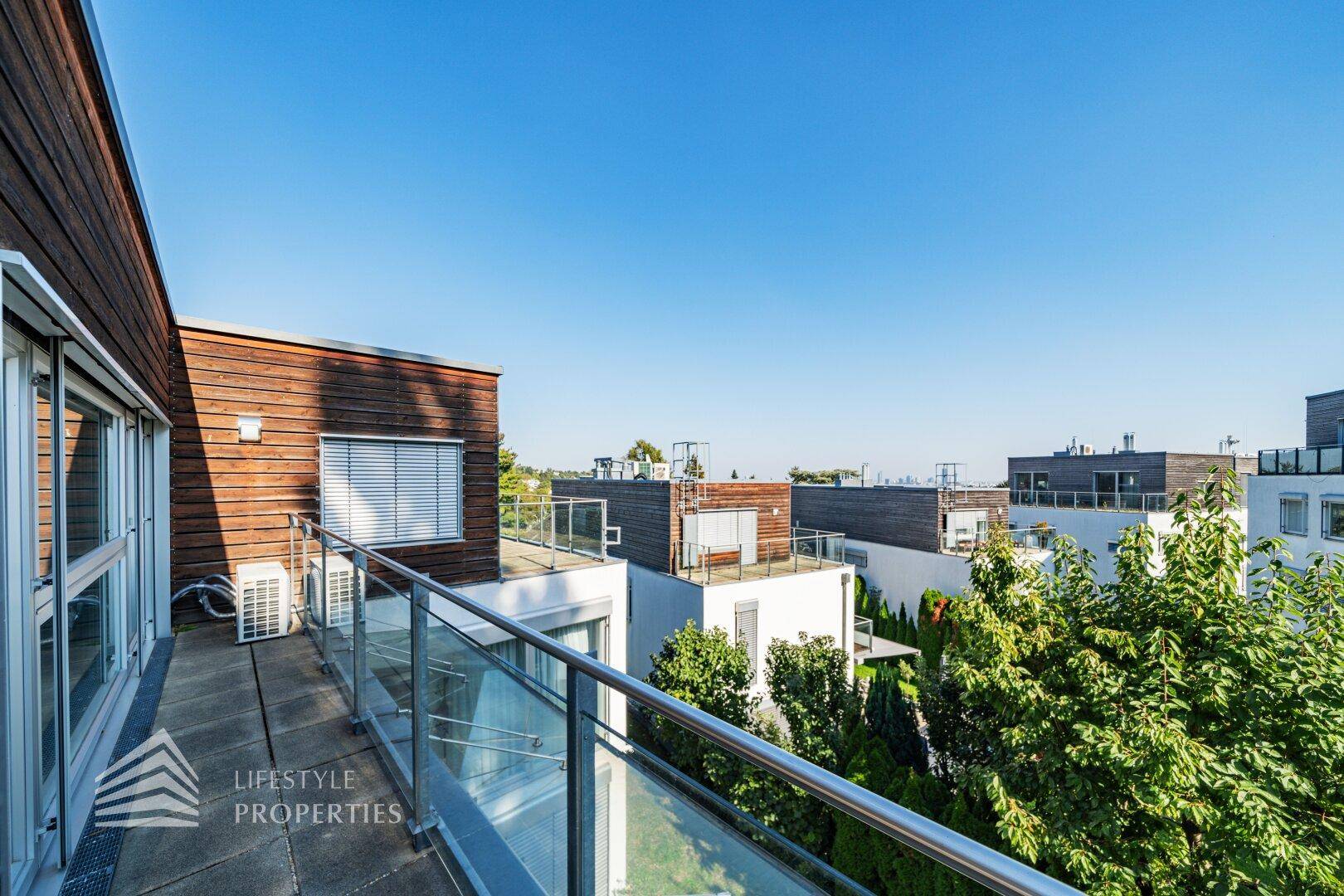 Geräumige Dachterrasse mit Holzelementen, Glasgeländer und Blick auf die Umgebung.