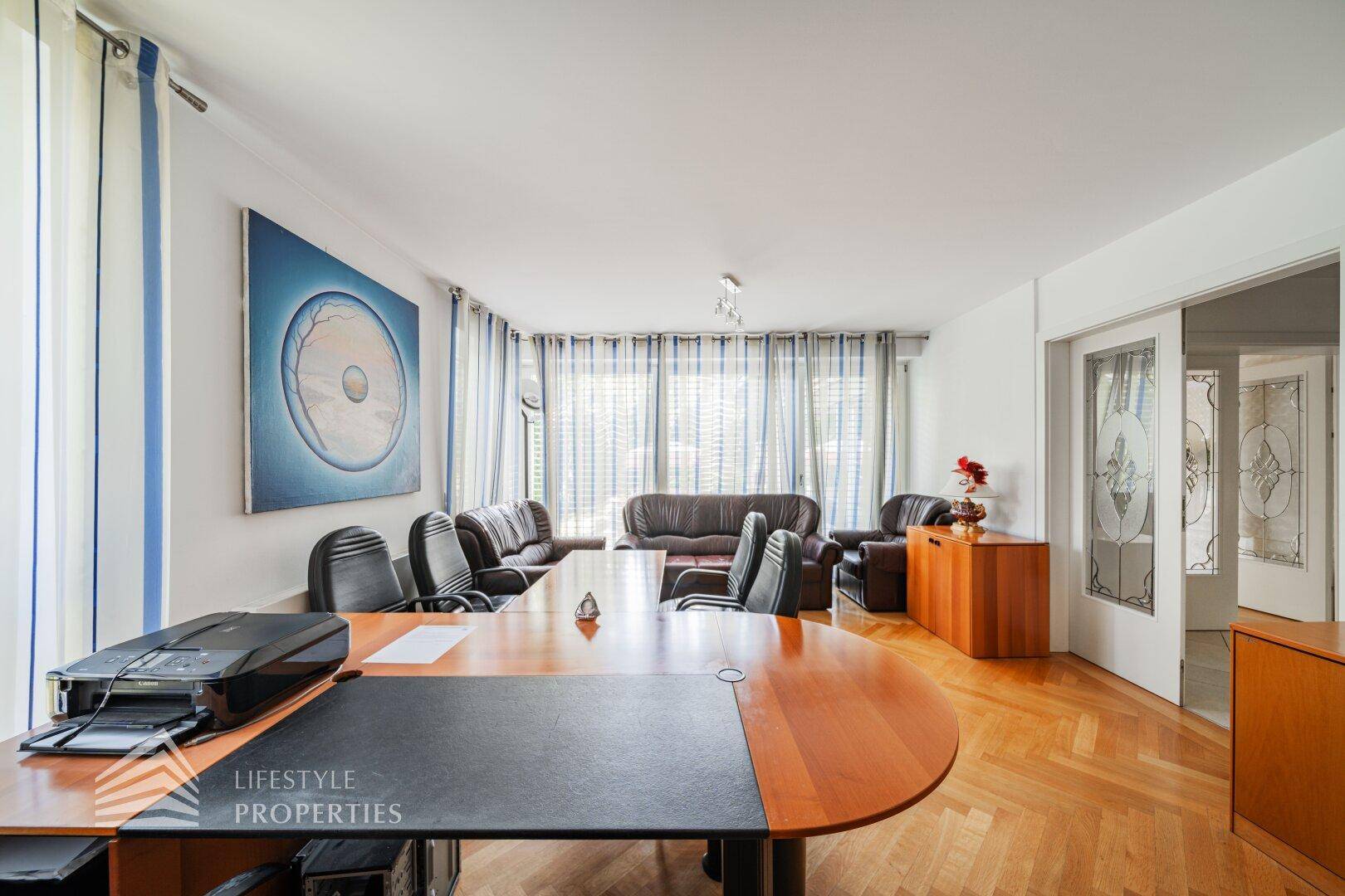 Helles Büro mit großem Schreibtisch, Ledersofas und viel Tageslicht.