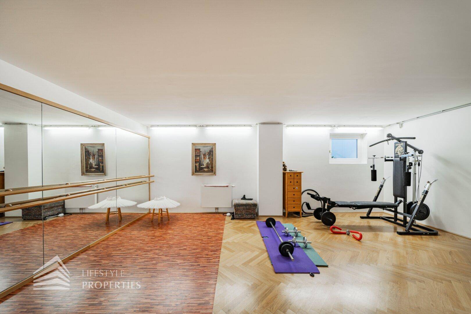 Großer Fitnessraum mit Spiegelwand, Ballettstange und verschiedenen Trainingsgeräten.