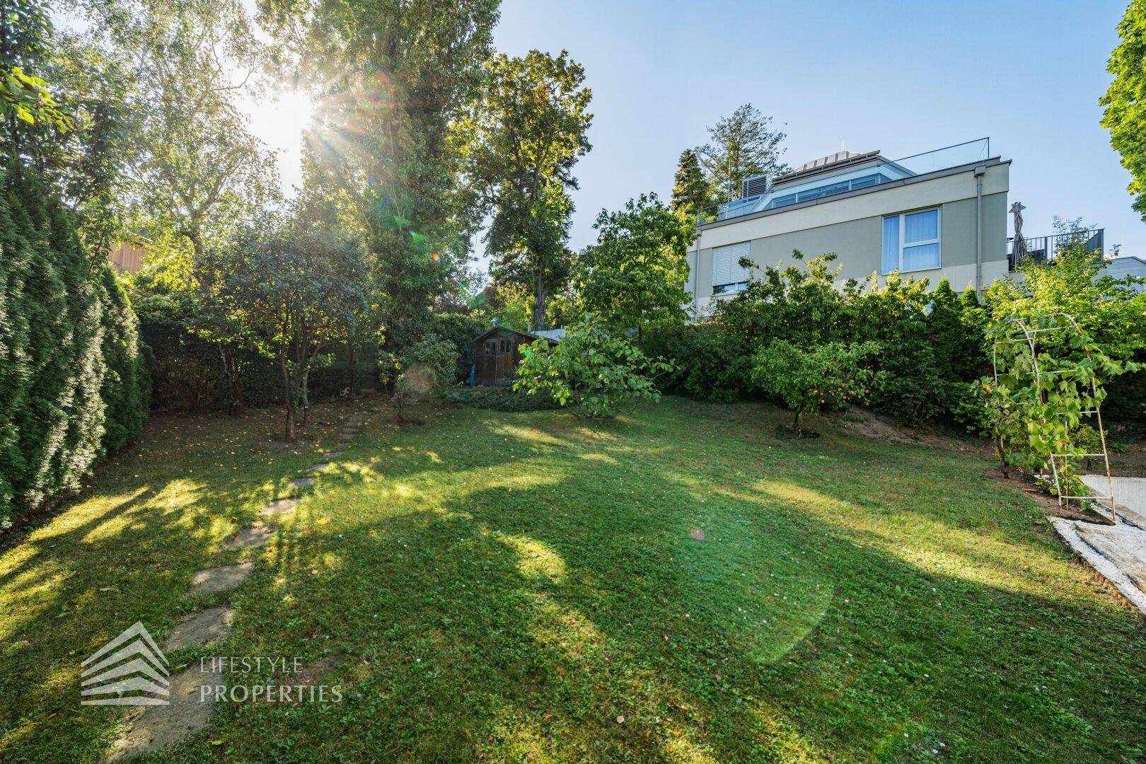 Sonniger Garten mit altem Baumbestand, Rasenfläche und einem kleinen Gartenhaus.
