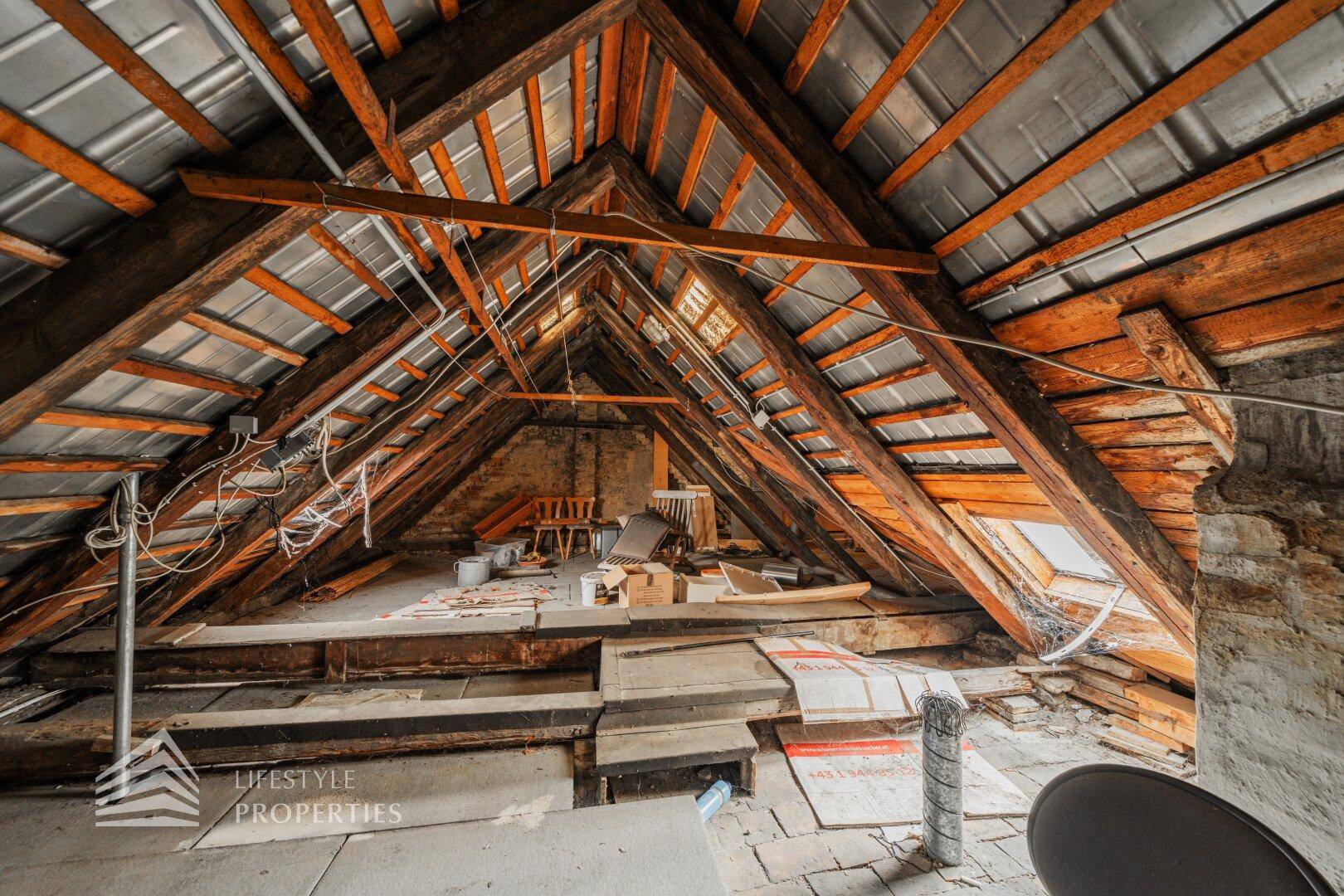 Unausgebauter Dachboden mit sichtbaren Holzbalken und Dachfenstern.