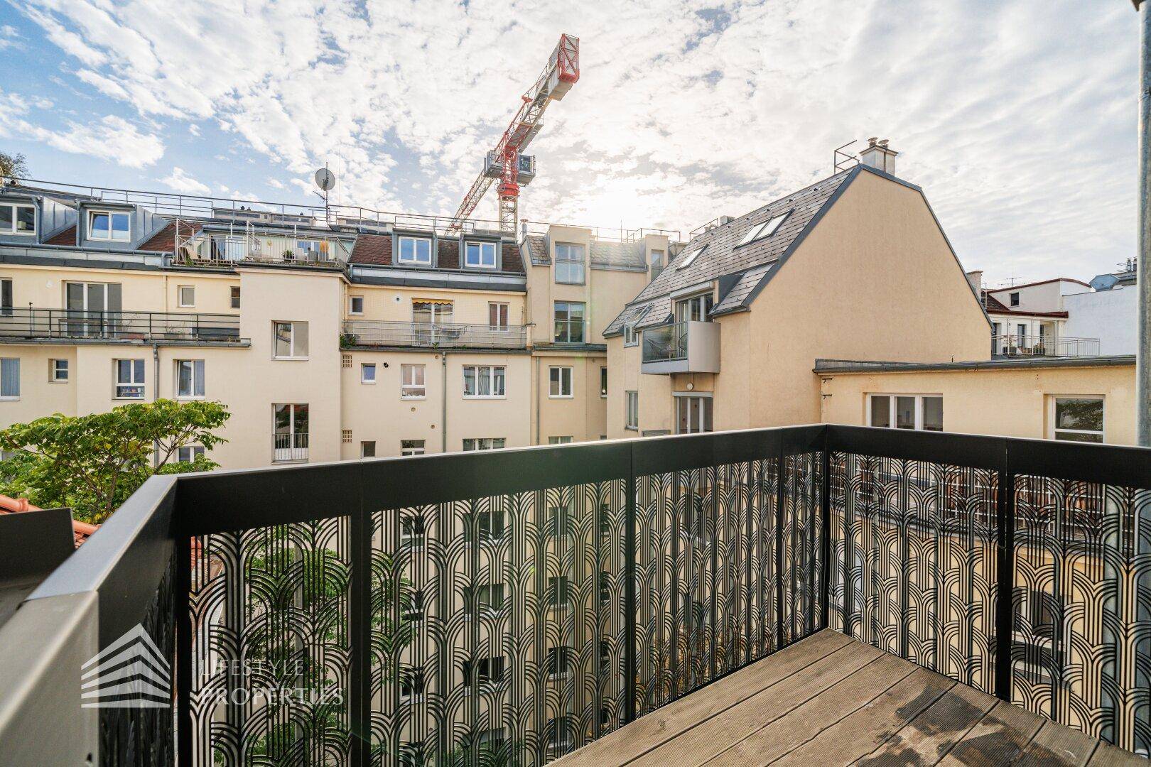 Sonniger Balkon mit Holzboden und modernem Geländer, bietet Blick auf die umliegenden Gebäude.