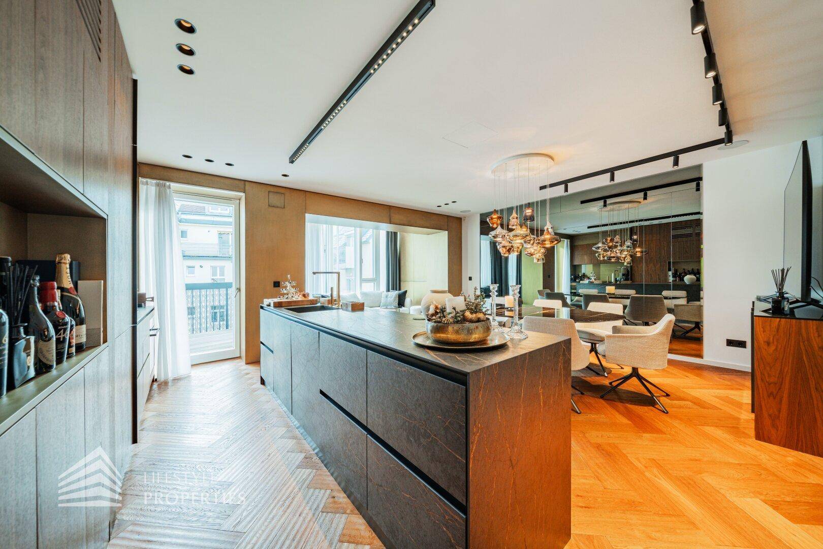 Moderne Küche mit Insel, Essbereich und Zugang zu einem Balkon, alles auf Fischgrätparkett.