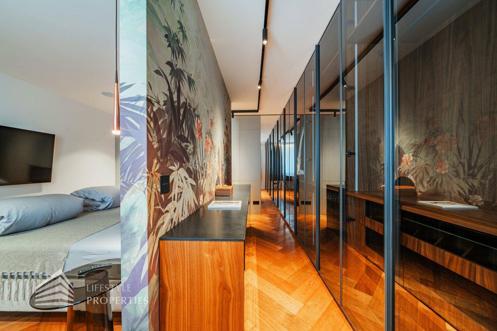 Geräumiger begehbarer Kleiderschrank mit eleganten Glasfronten und floraler Wandgestaltung.