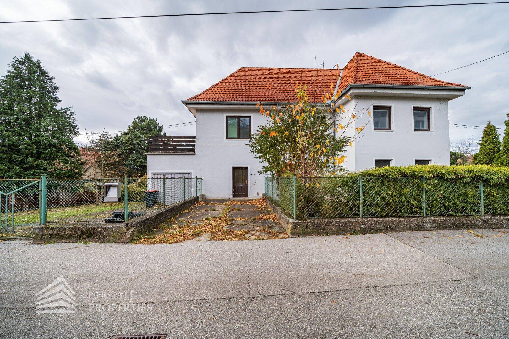 Vorderansicht des Hauses mit weißer Fassade, rotem Ziegeldach und Garagenzufahrt.
