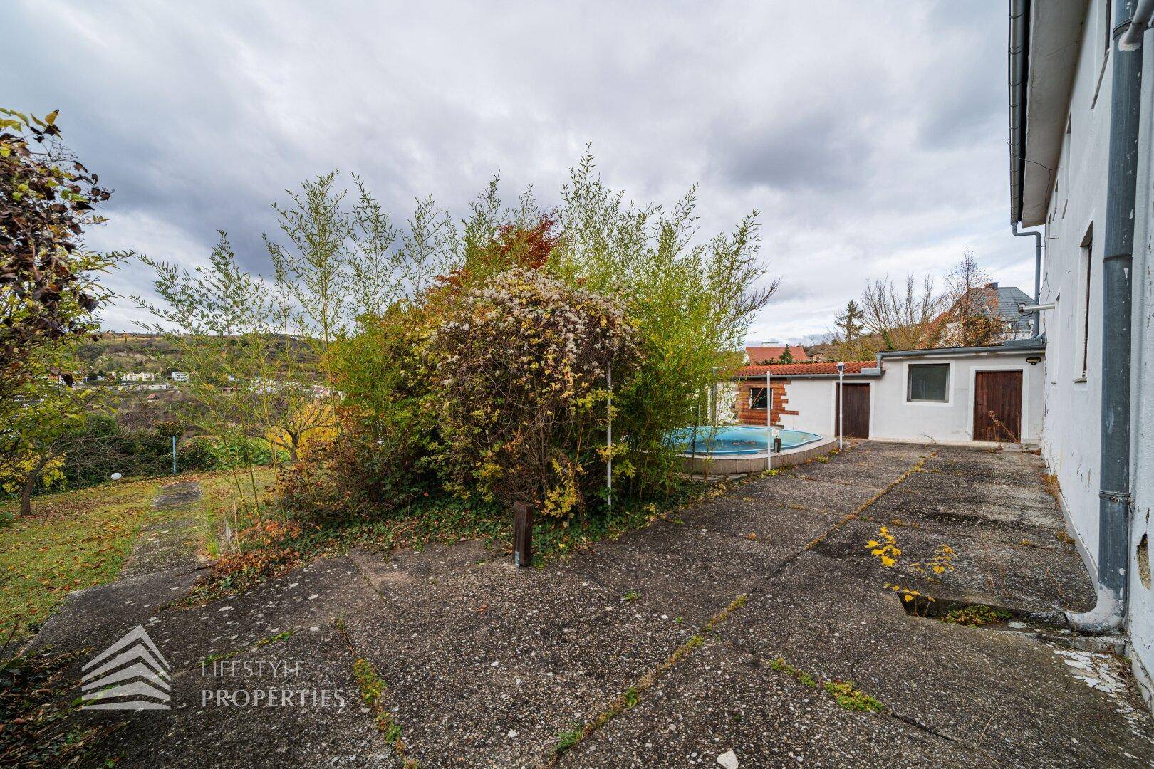 Gepflasterter Bereich neben dem Haus mit kleinem Pool und Nebengebäuden.