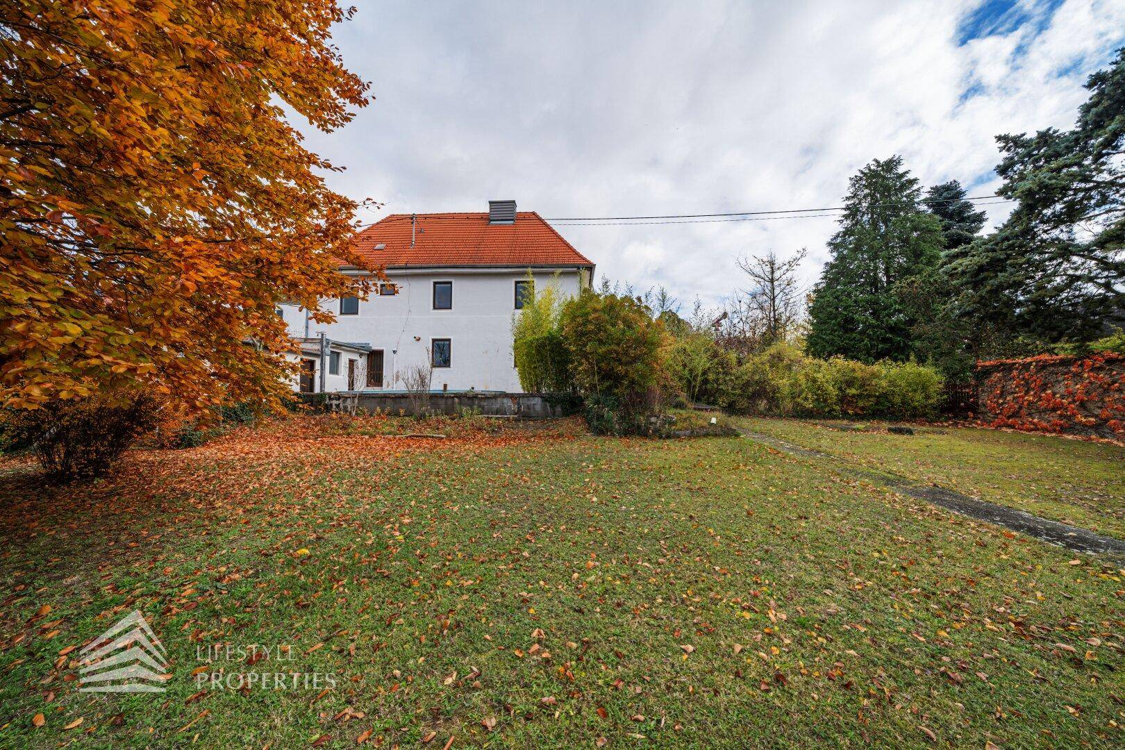 Weitläufiger Garten mit Rasenfläche, Herbstlaub und Blick auf die Hausfassade.
