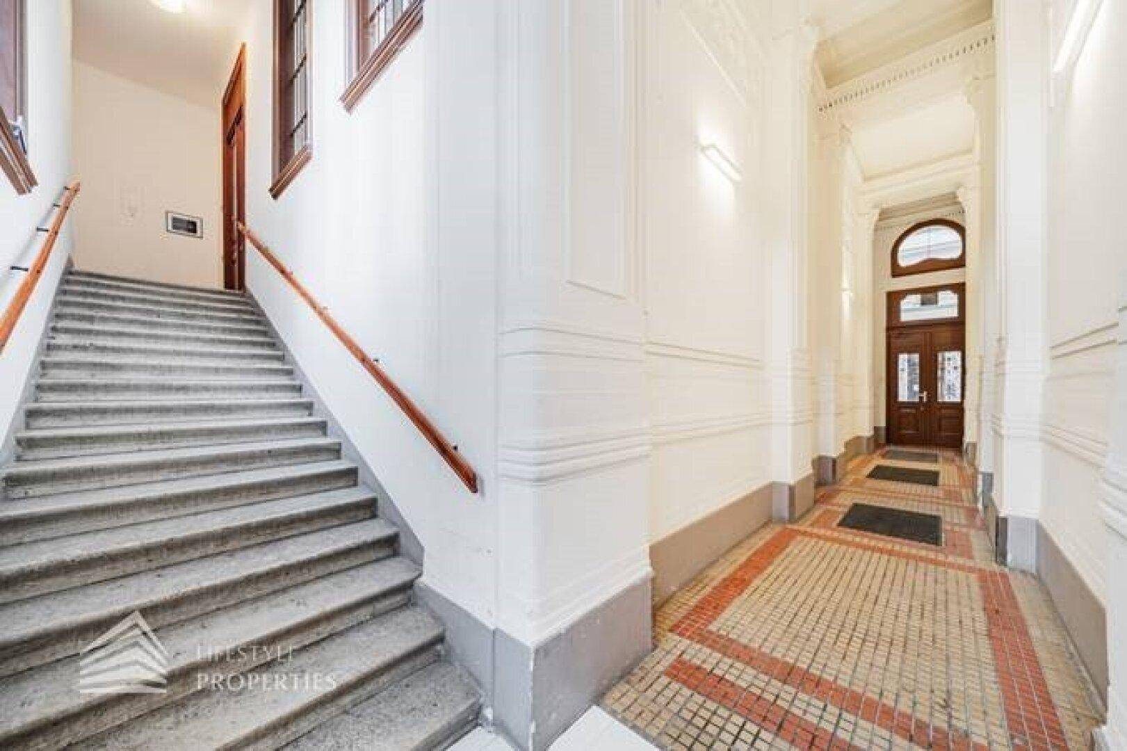 Elegantes Treppenhaus mit Holzgeländer und gemustertem Fliesenboden, führt zu den oberen Etagen.