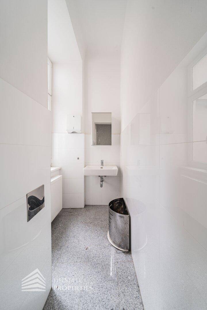 Heller Toilettenraum mit Waschbecken, Spiegel und Fenster, ausgestattet mit weißen Fliesen.