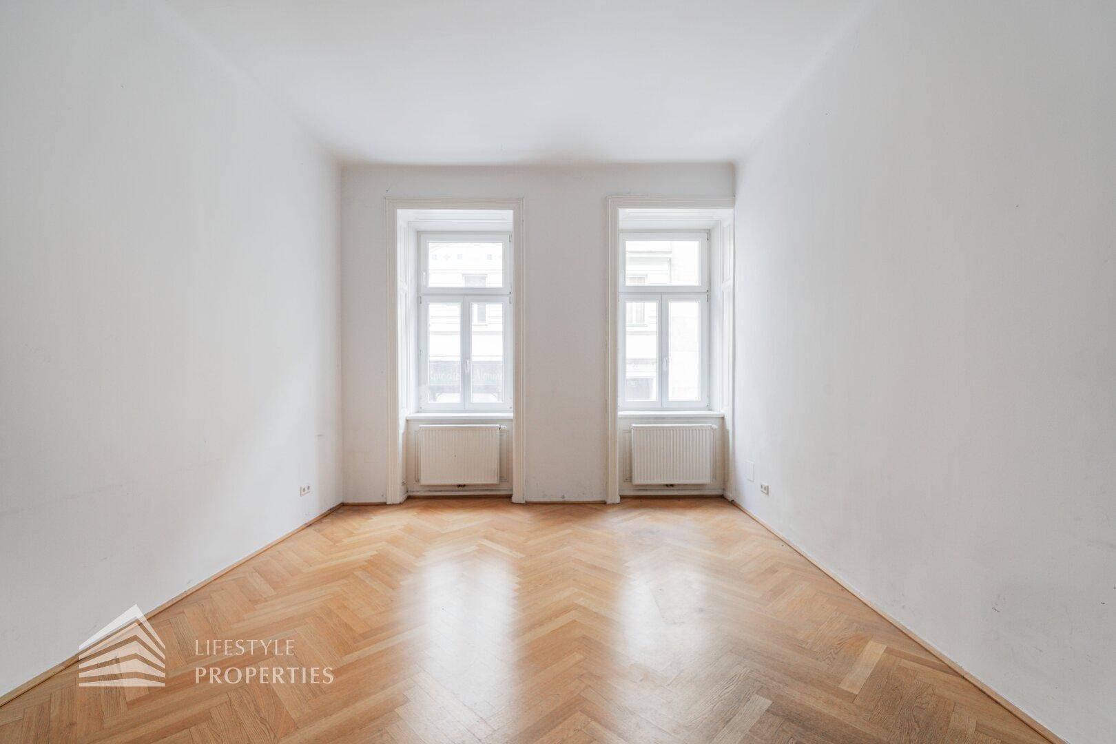 Geräumiger Raum mit Fischgrätparkett und zwei großen Fenstern, ideal für ein helles Büro.