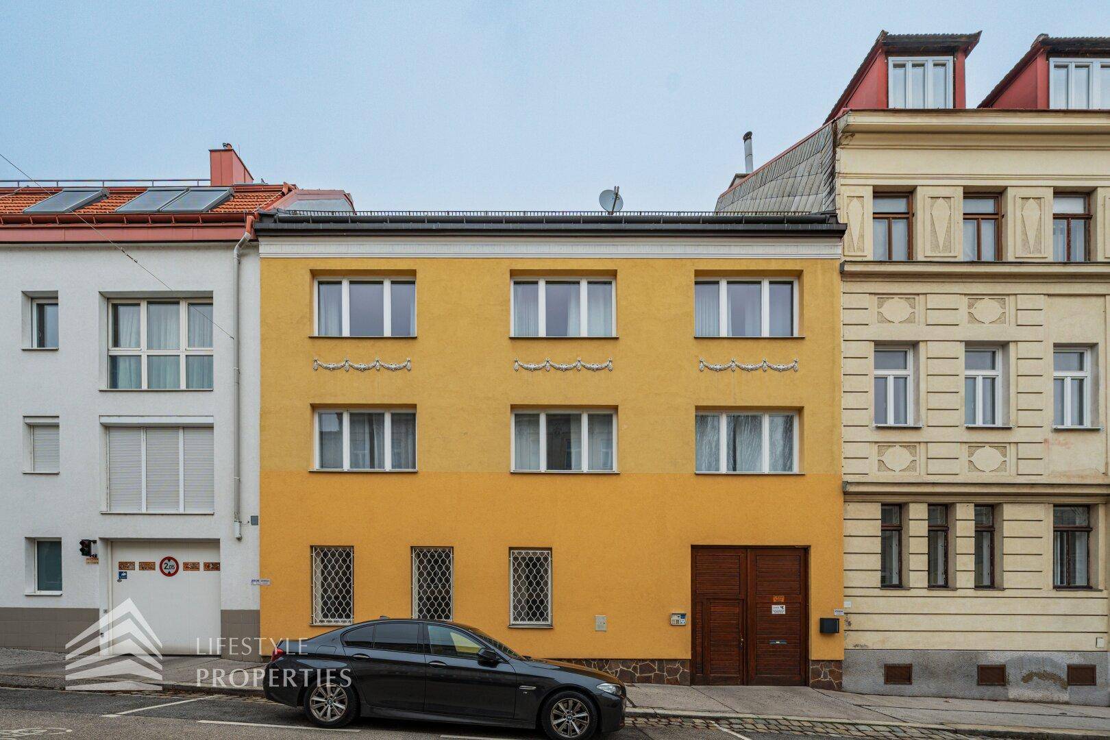 Fassade eines gelben Wohnhauses mit mehreren Fenstern und Holztor.